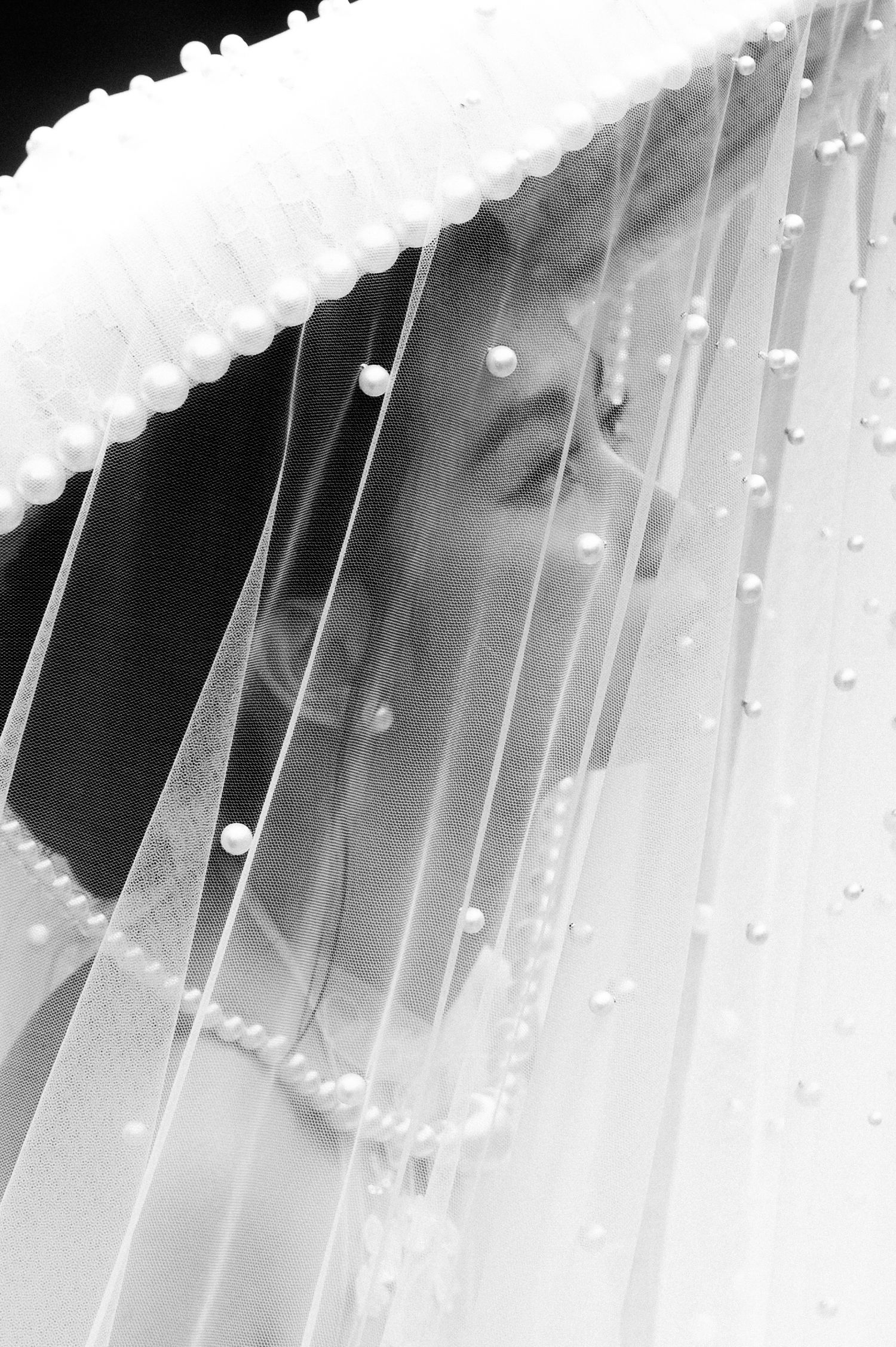 Black and white photo of a bride wearing a pearl-trimmed wedding veil, her eyes closed in a serene moment.