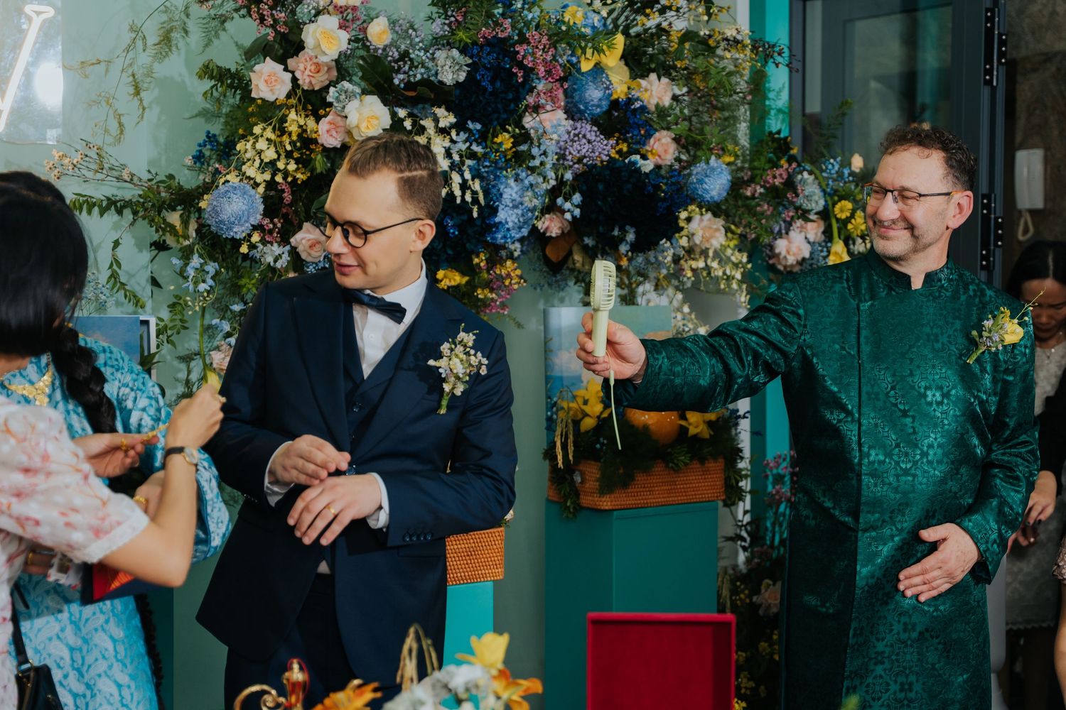Two grooms celebrate their wedding ceremony with guests, surrounded by colorful floral arrangements.