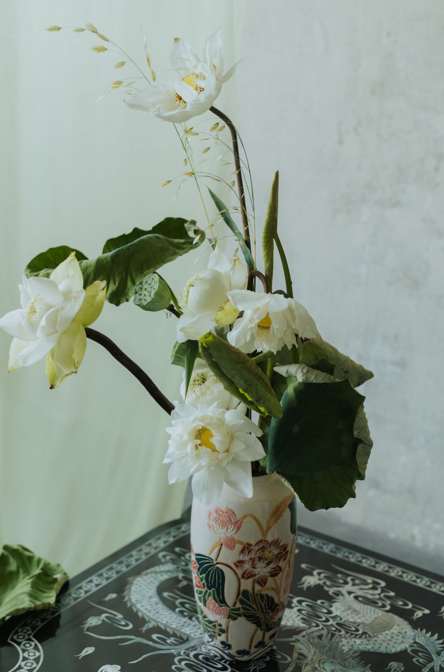 White lotus flowers arranged in a decorative Asian ceramic vase on a dark table with dragon motif.