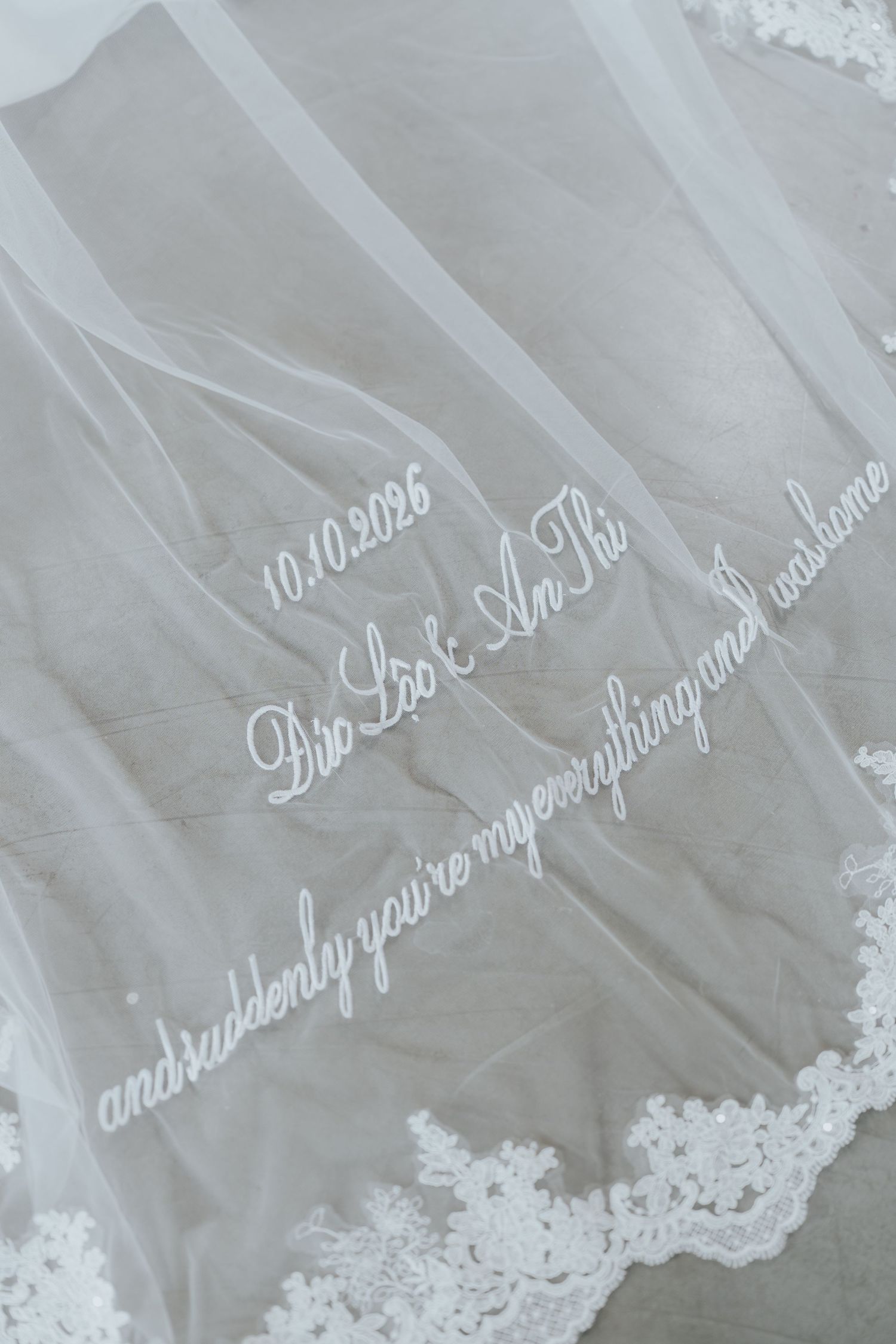 White wedding veil with embroidered date 10.10.2026, names Dio Leo & An Thi, and romantic quote in delicate script.