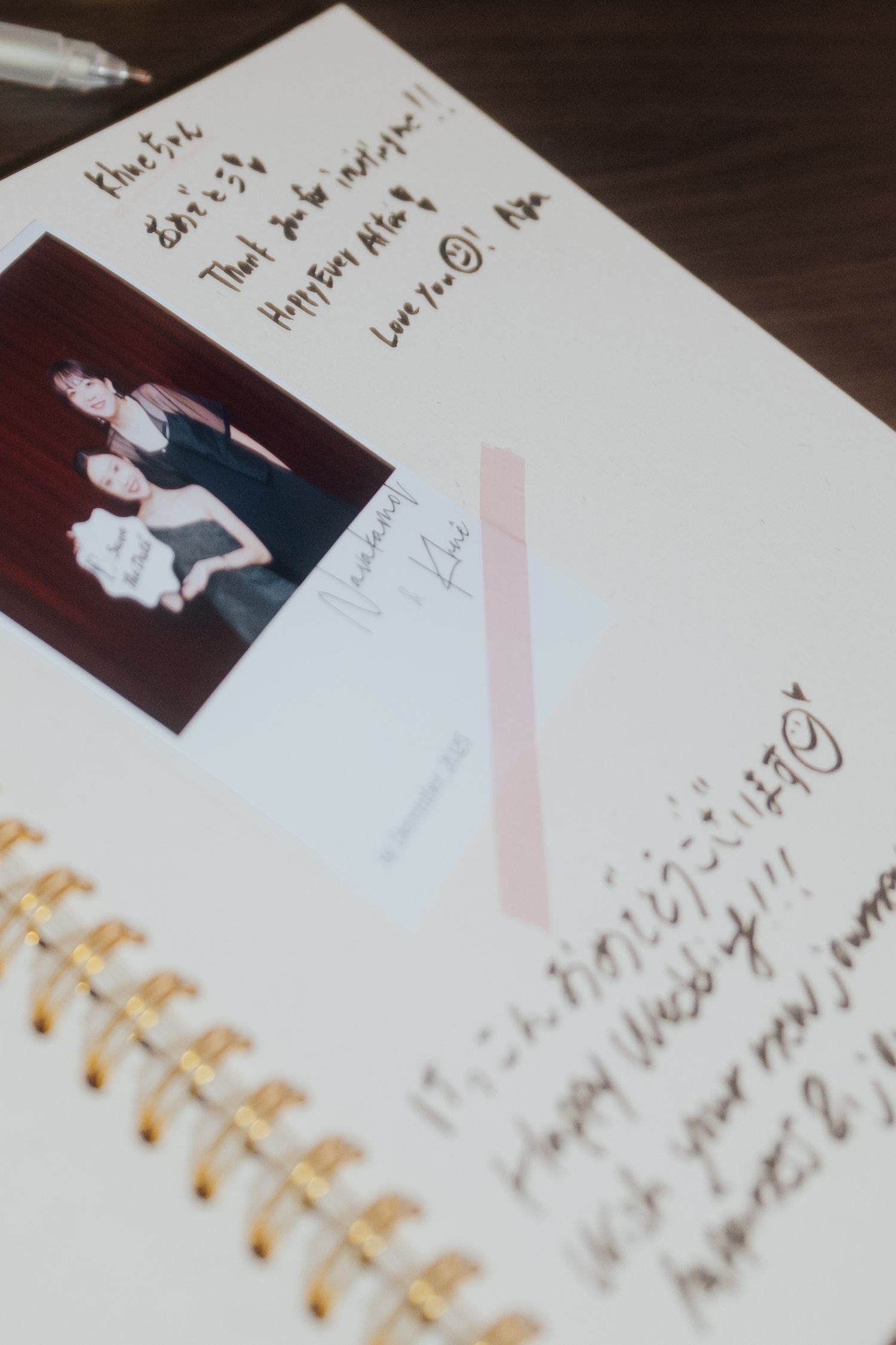 A spiral notebook with handwritten messages, a Polaroid photo of two women, and gold leaf binding decorations.