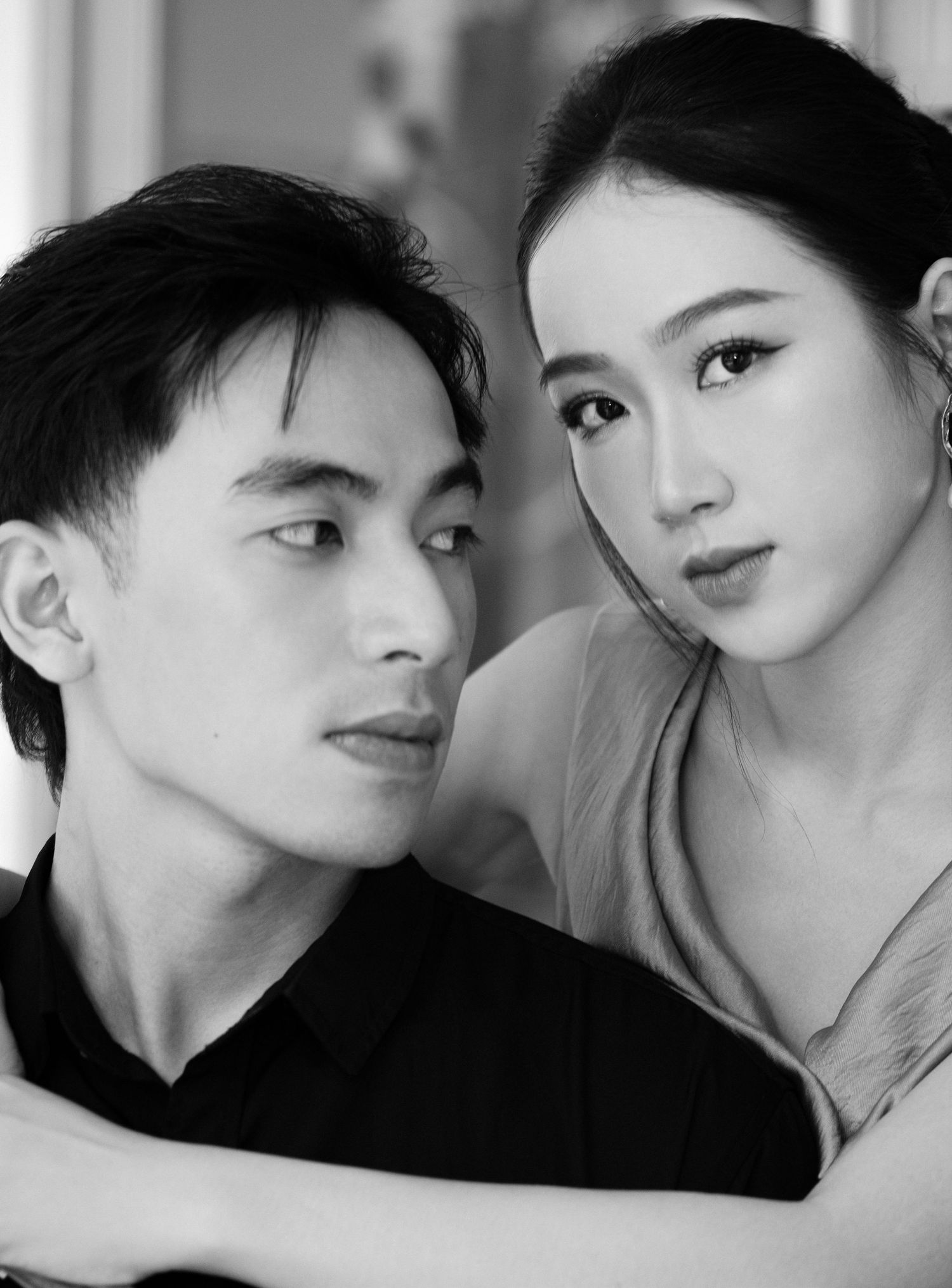 Black and white portrait of a young Asian couple posing intimately, woman resting chin on mans shoulder, studio photo.