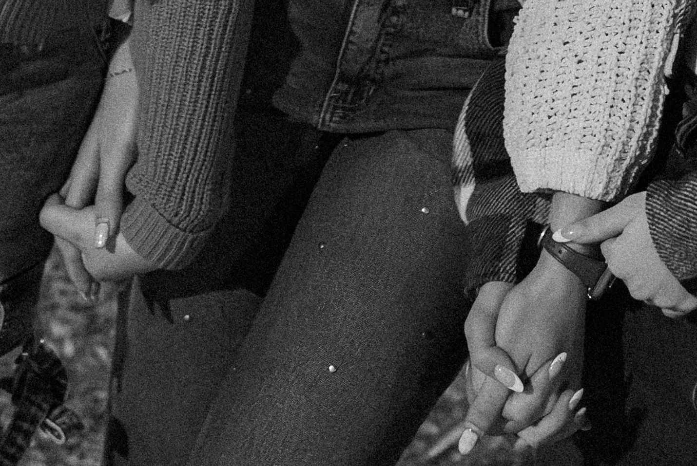 Black and white photo of two people holding hands, wearing casual sweaters and jeans outdoors.