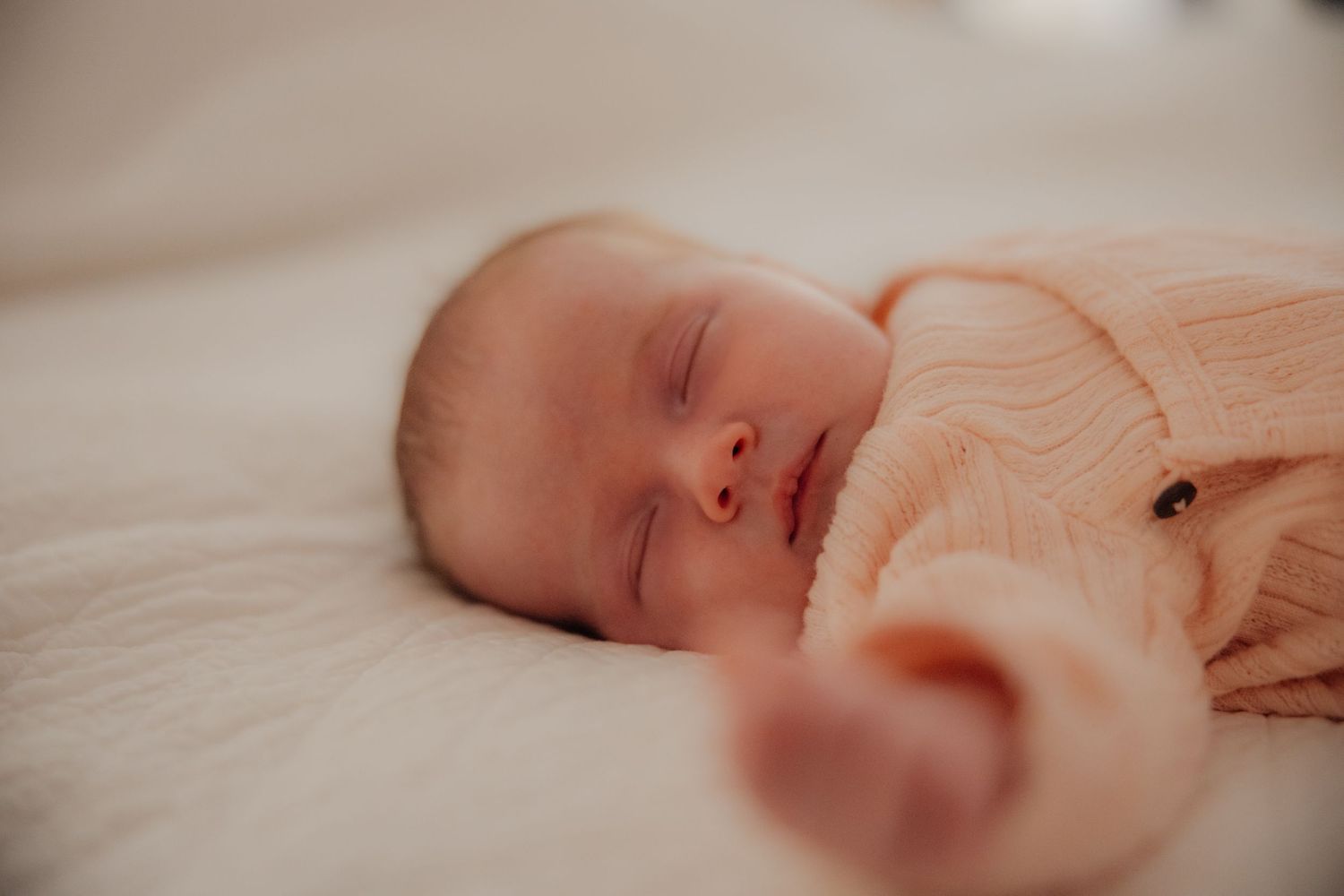 Peaceful newborn baby sleeping soundly in a soft pink onesie on a white blanket.