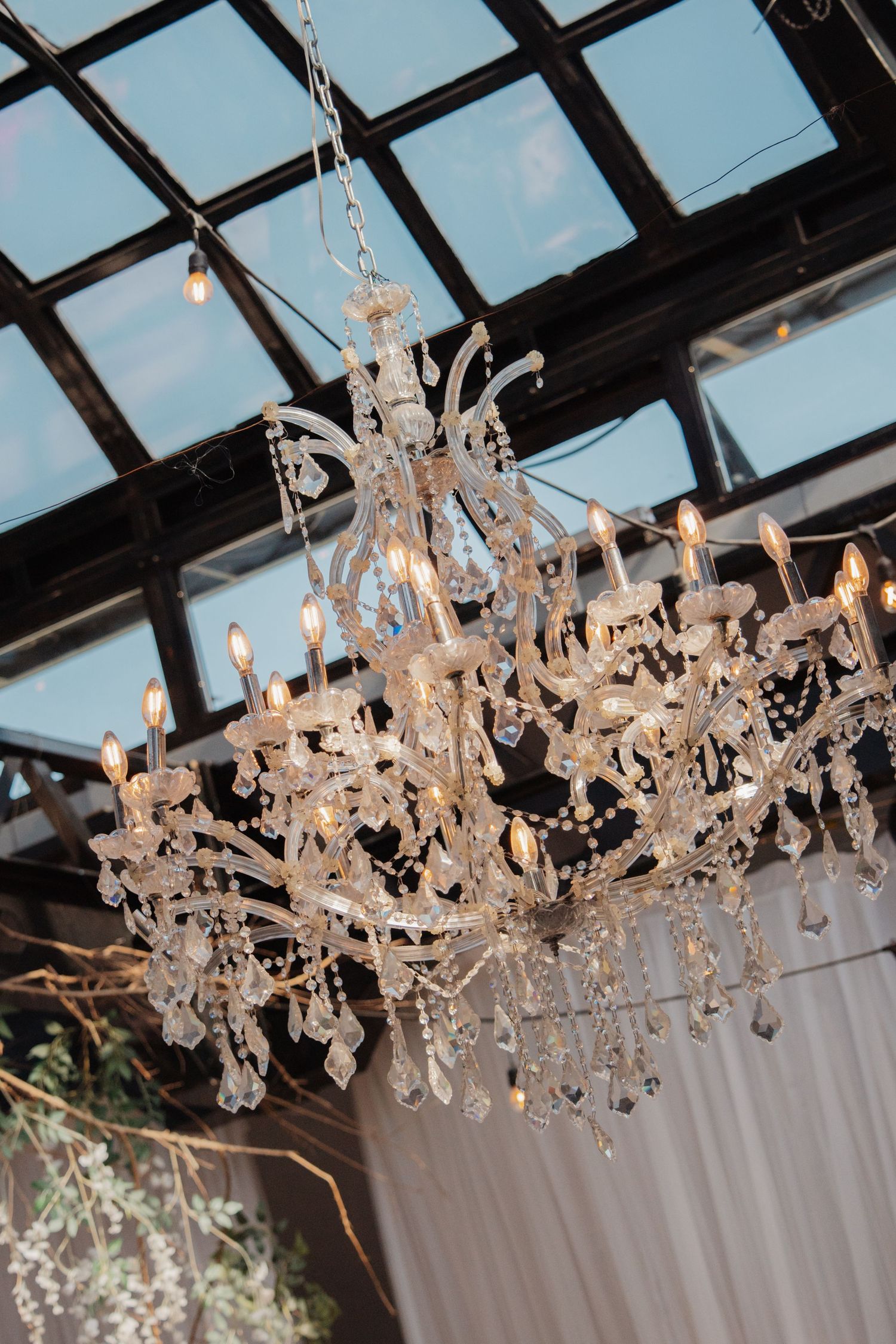 Elegant crystal chandelier with candle lights hanging in a glass-ceiling wedding reception venue.