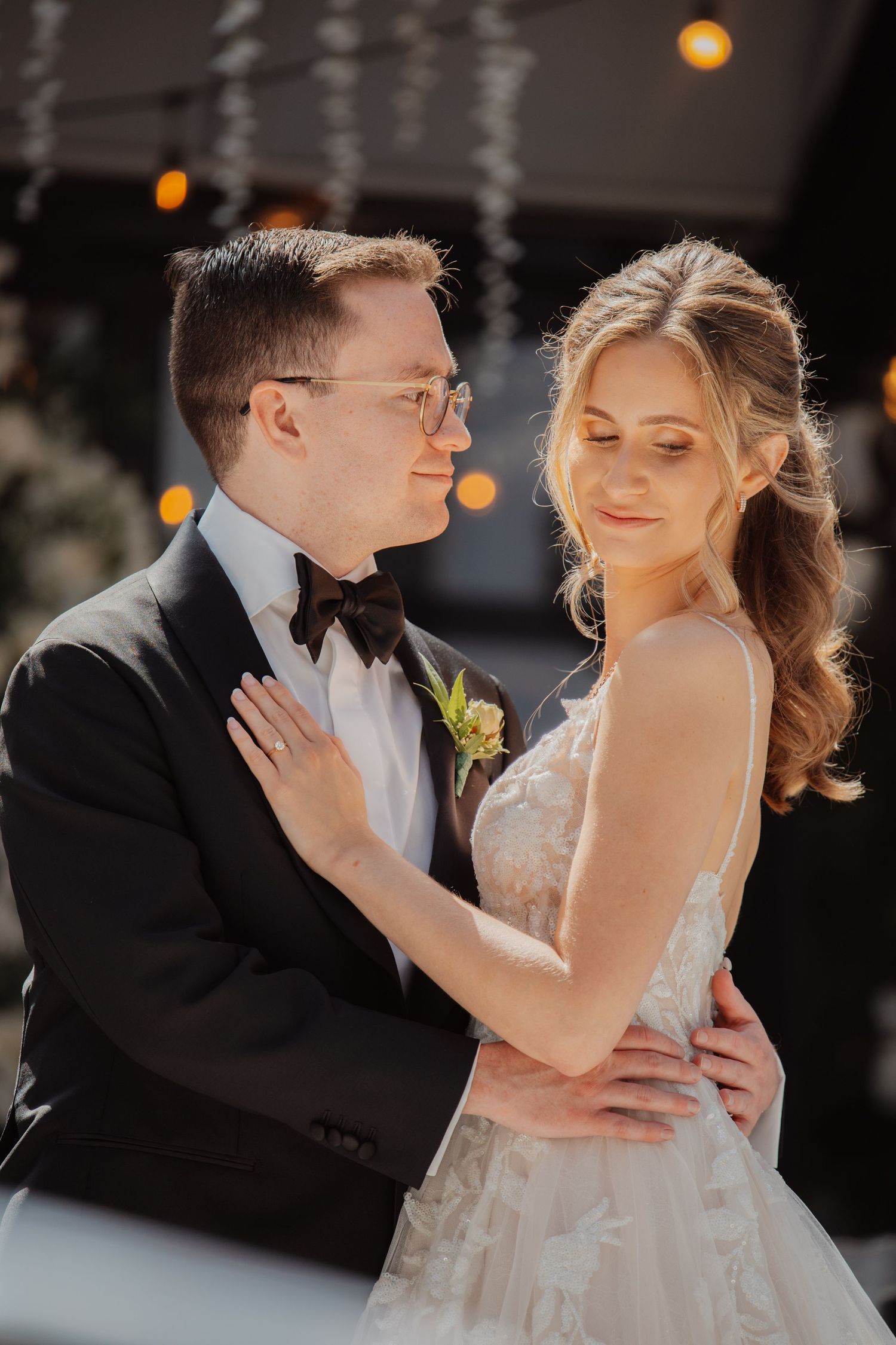 Bride in spaghetti strap lace gown and groom in black tuxedo share a tender moment.