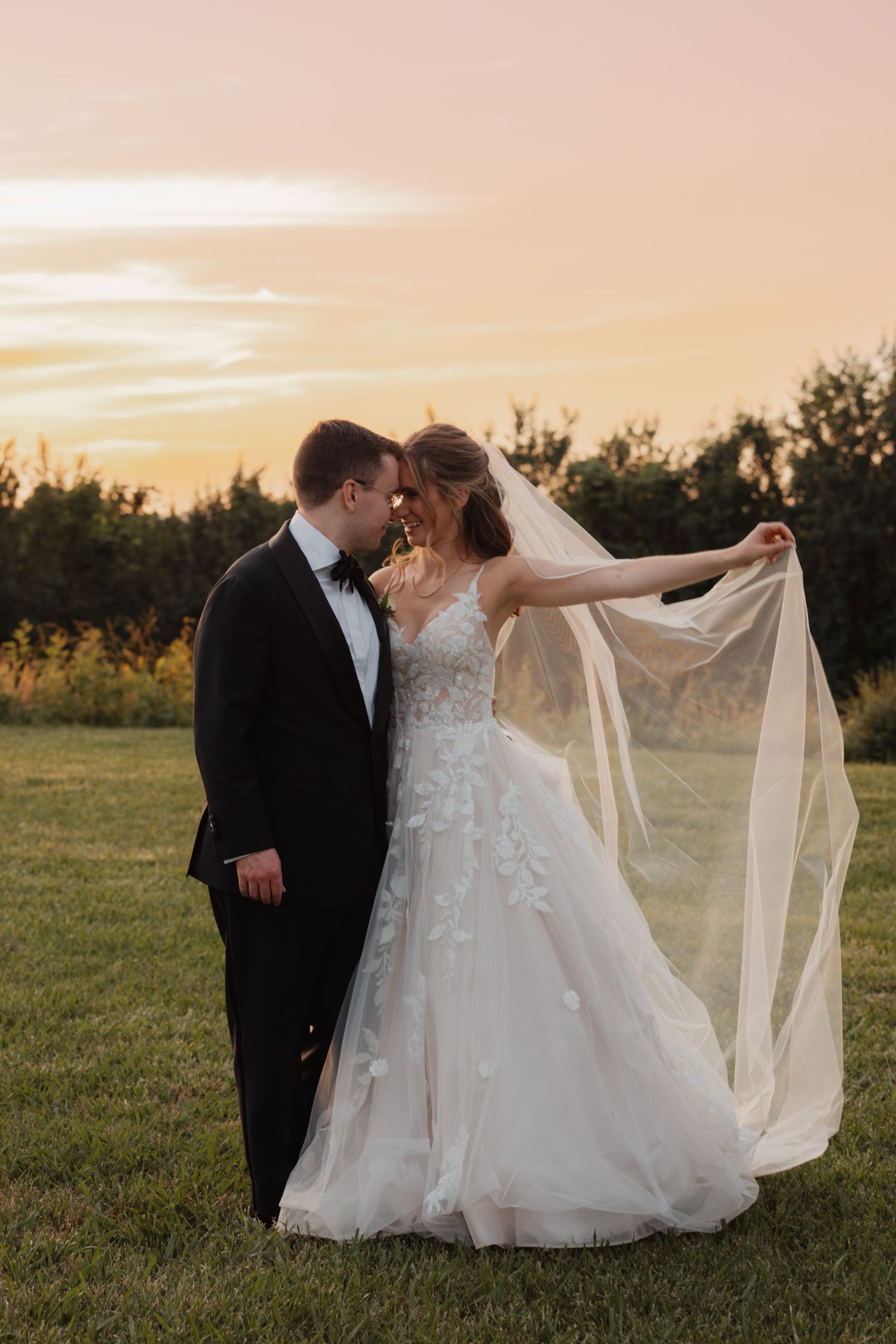 Bride and groom sharing romantic sunset moment outdoors, with veil flowing in the golden light.