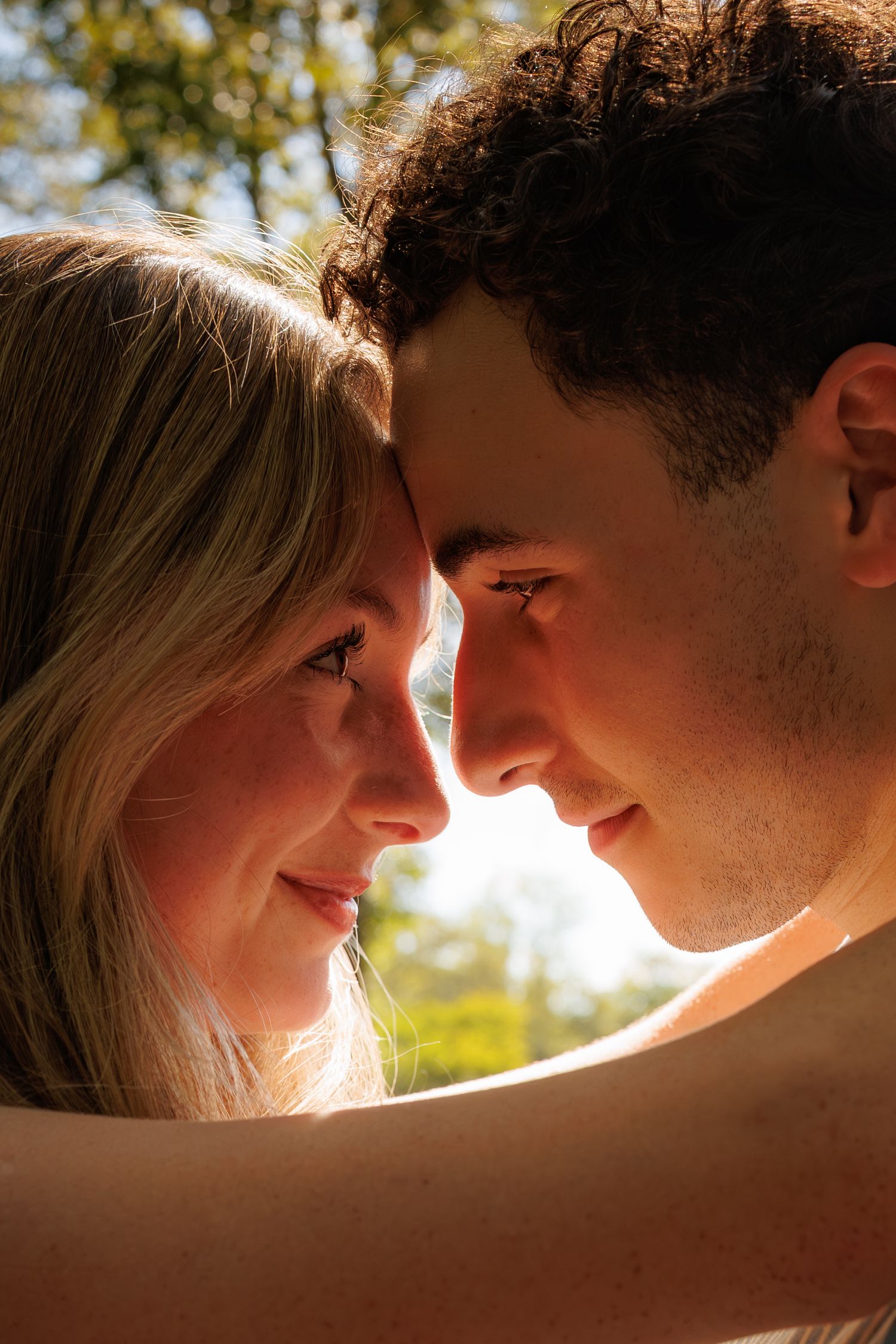 A close-up of a smiling couple touching foreheads in warm golden sunlight outdoors.