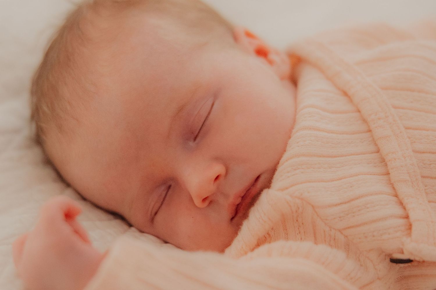 Peaceful newborn baby sleeping soundly wrapped in a soft pink knit blanket on a white surface.