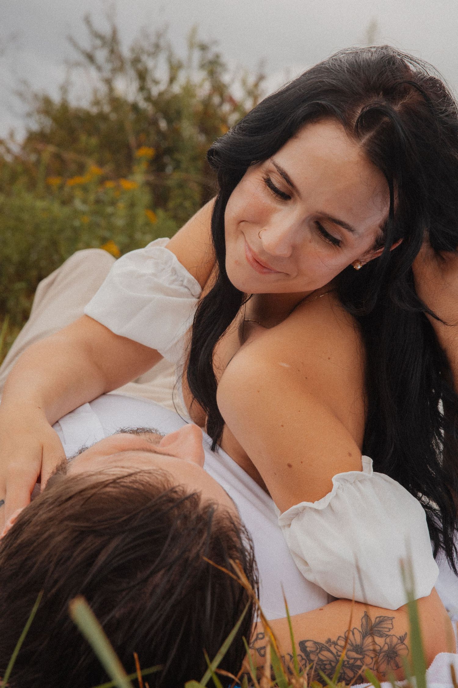 Woman with long dark hair smiling down at partner lying in her lap in a wildflower field.