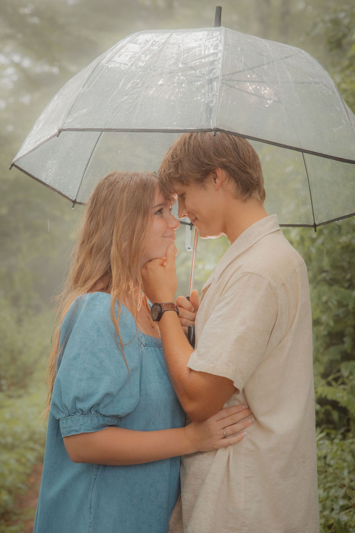 Young couple standing close under a clear umbrella in a foggy forest, almost kissing.