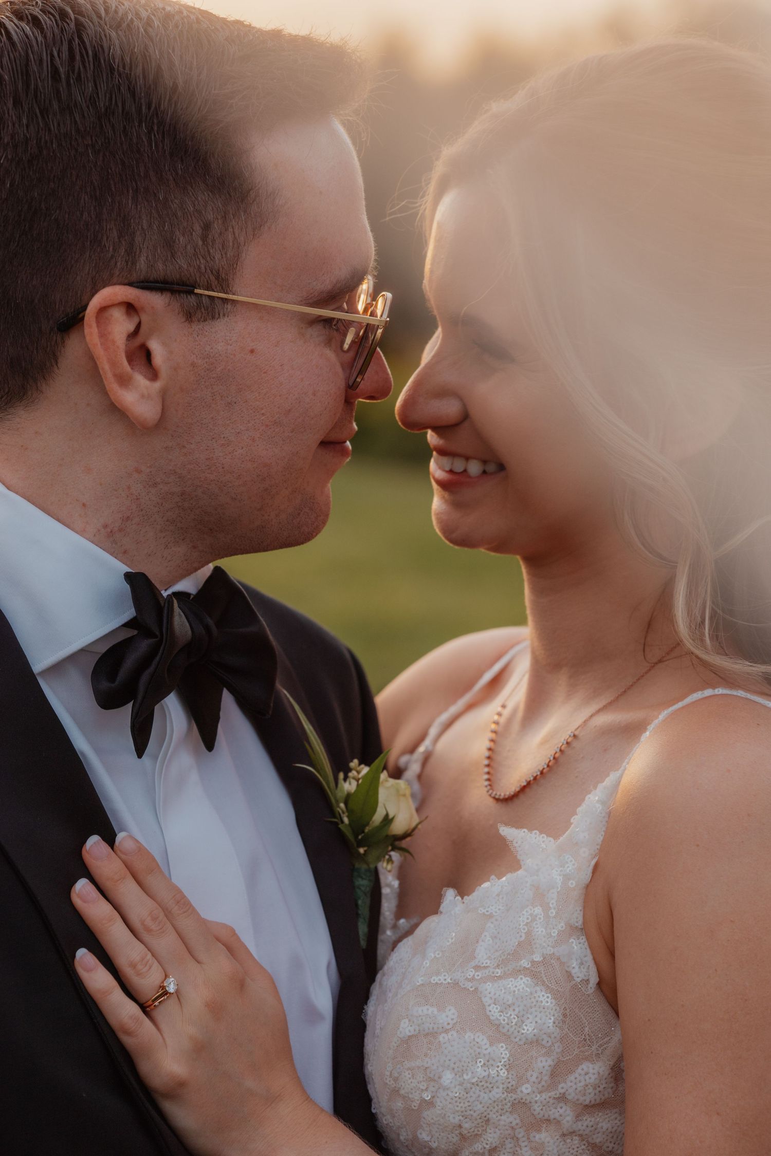 Close-up of smiling bride and groom touching foreheads in warm golden sunset light outdoors.