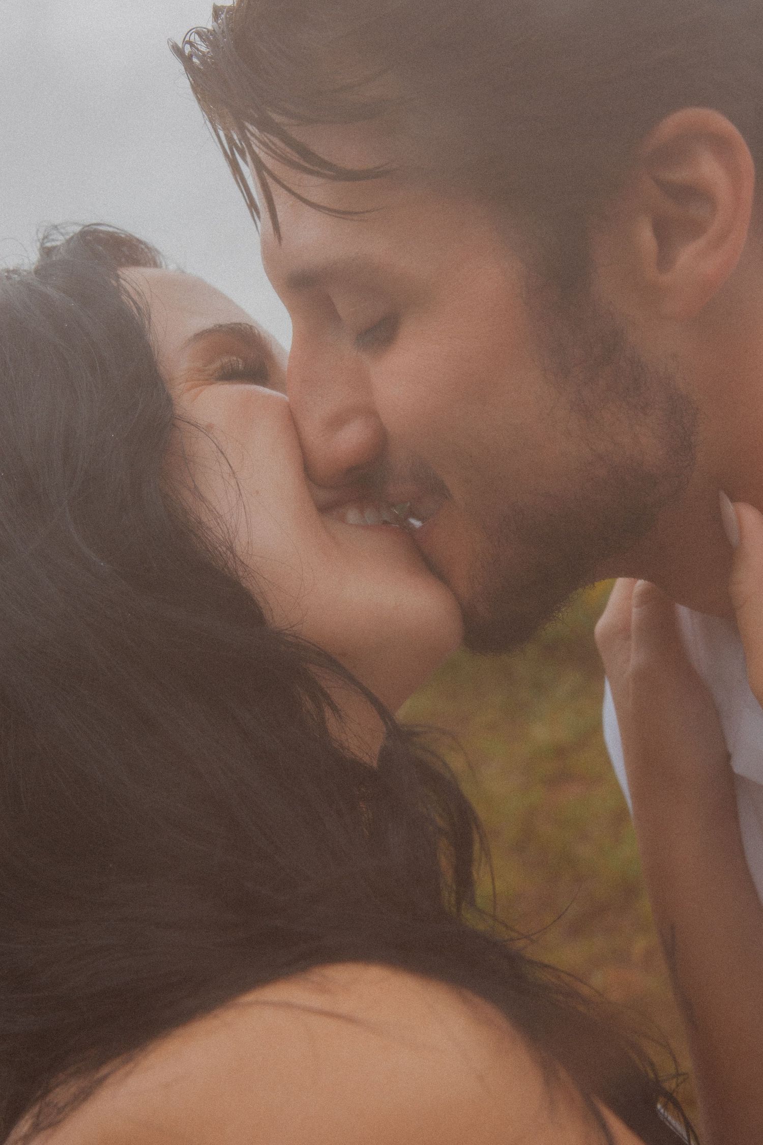 Close-up of couple sharing a tender kiss outdoors in soft foggy natural light.