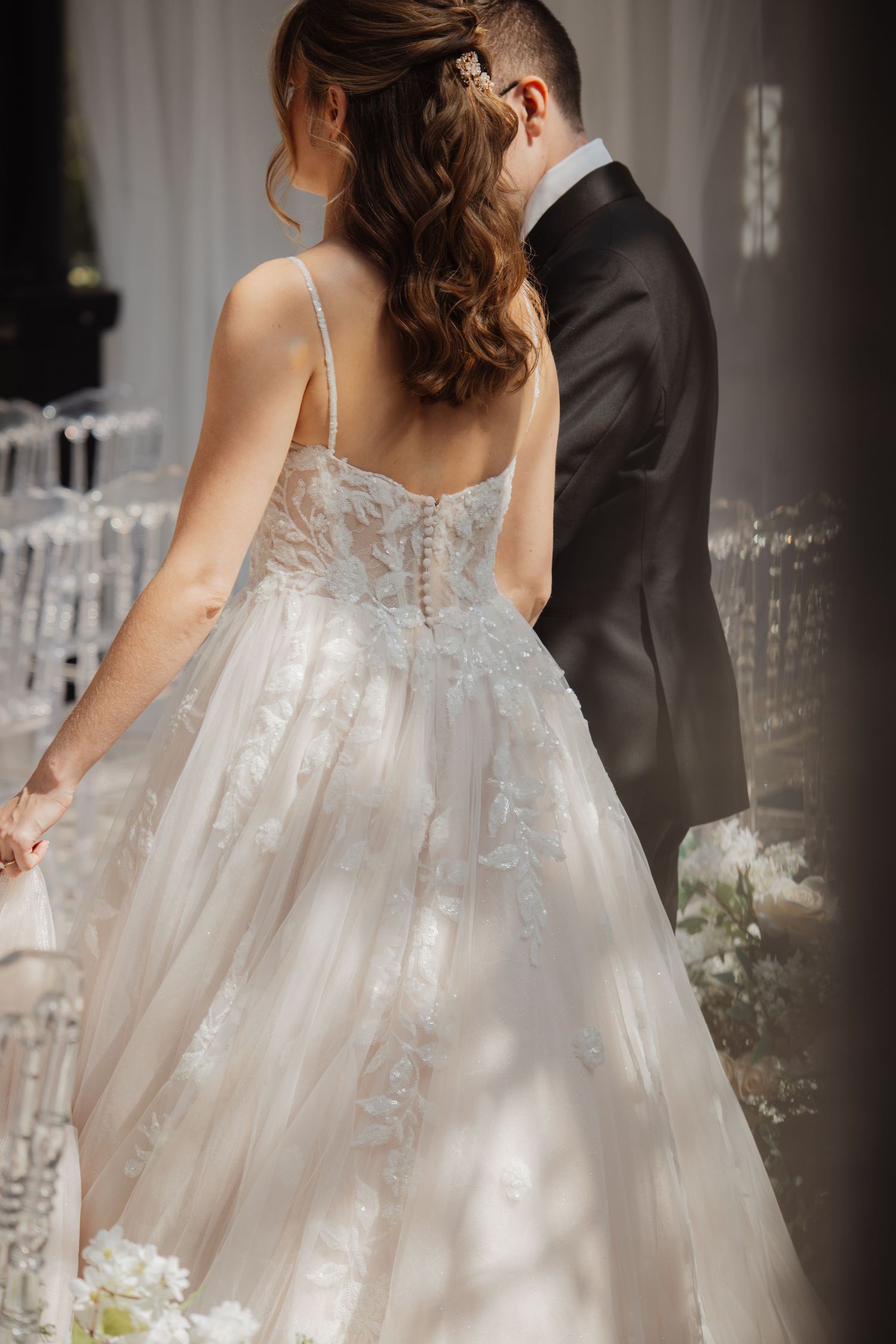 Back view of bride in lace corset wedding gown with elegant half-up hairstyle and groom.