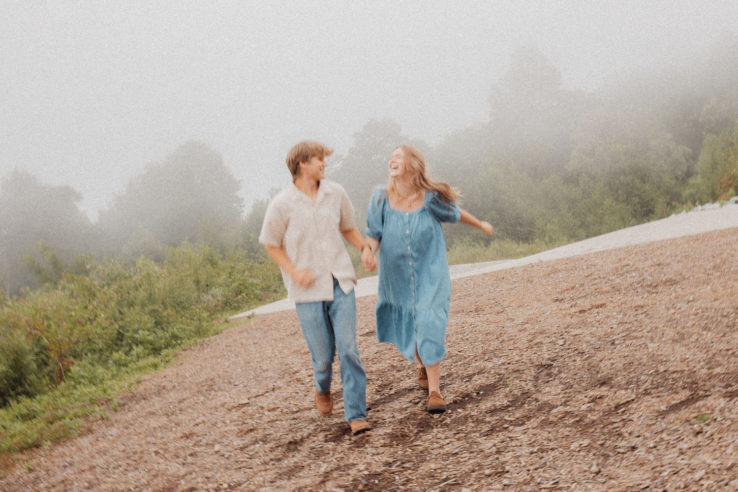 Couple walks hand in hand along a misty mountain path surrounded by lush greenery.