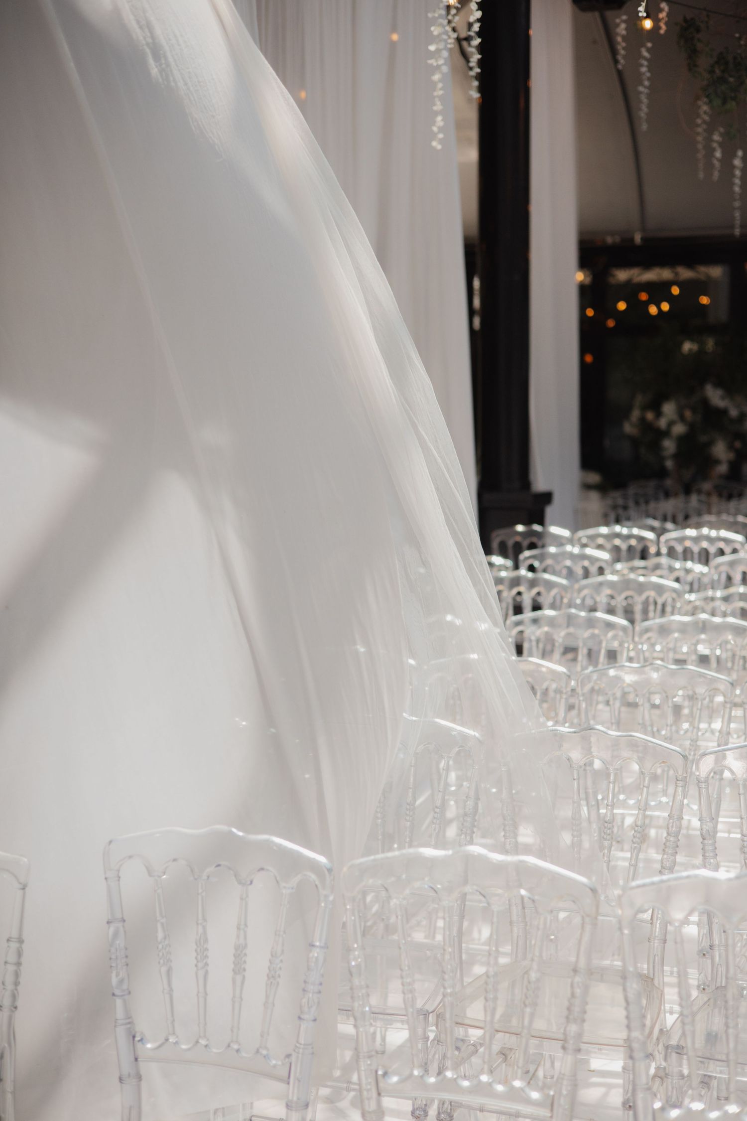 Elegant wedding ceremony setup with flowing white drapes and clear ghost chairs arranged in rows.