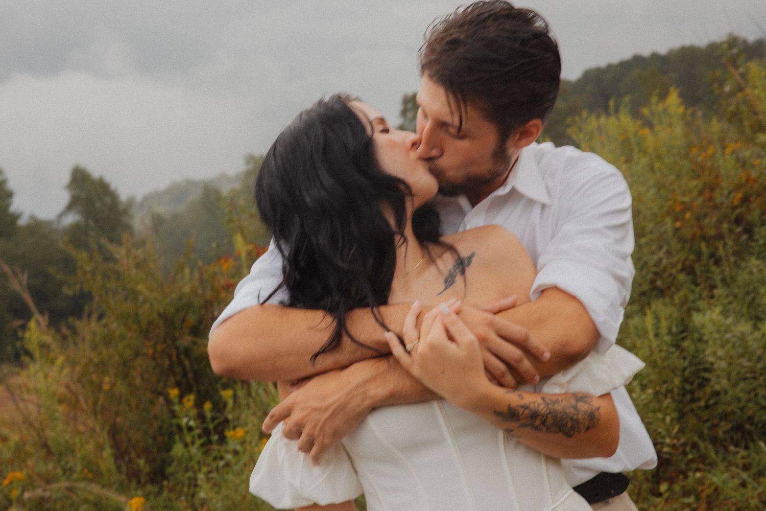 Couple sharing a passionate kiss outdoors surrounded by lush green foliage.