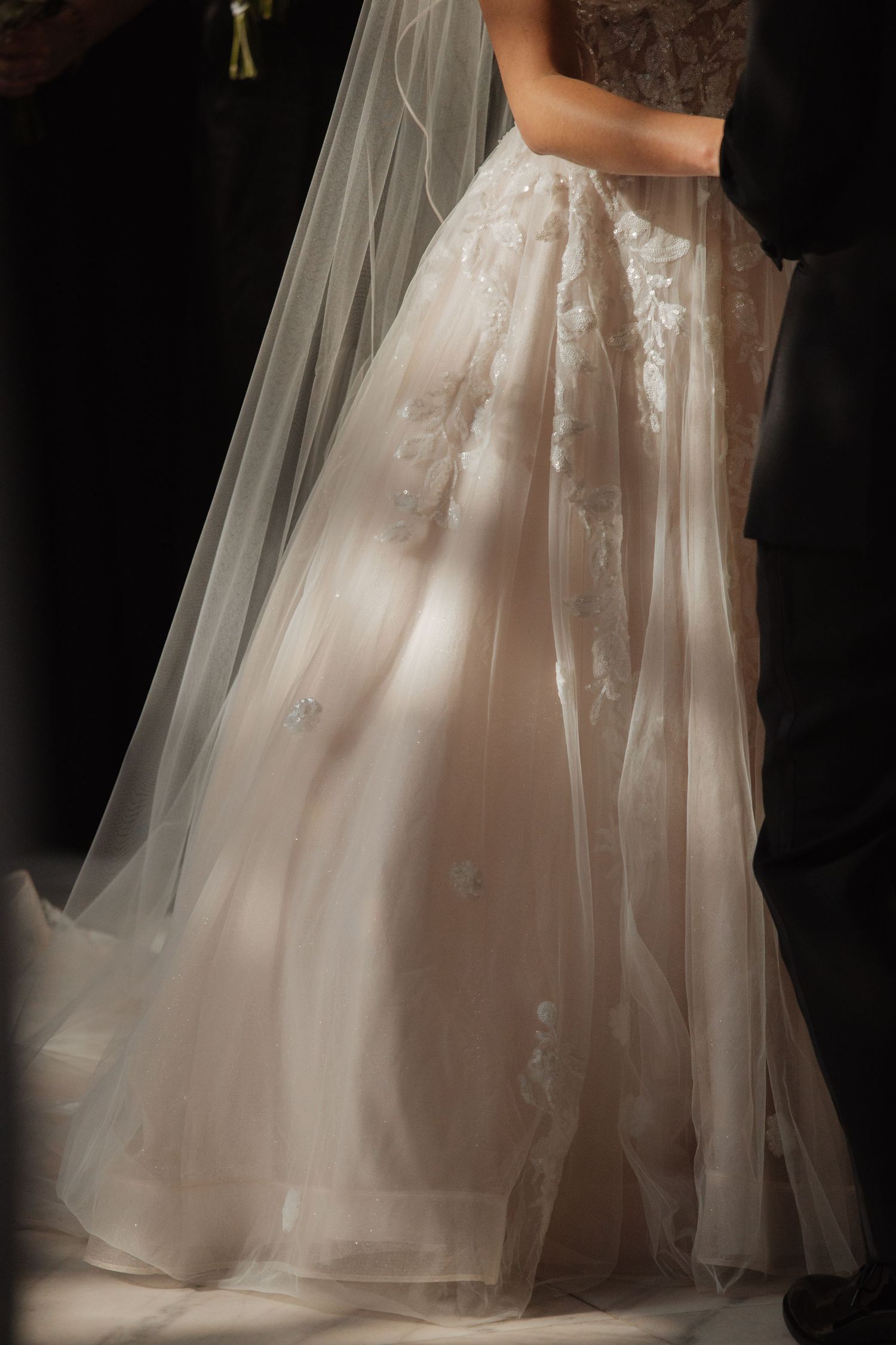 Close-up of bride's elegant lace and tulle wedding gown with flowing veil in soft natural light.