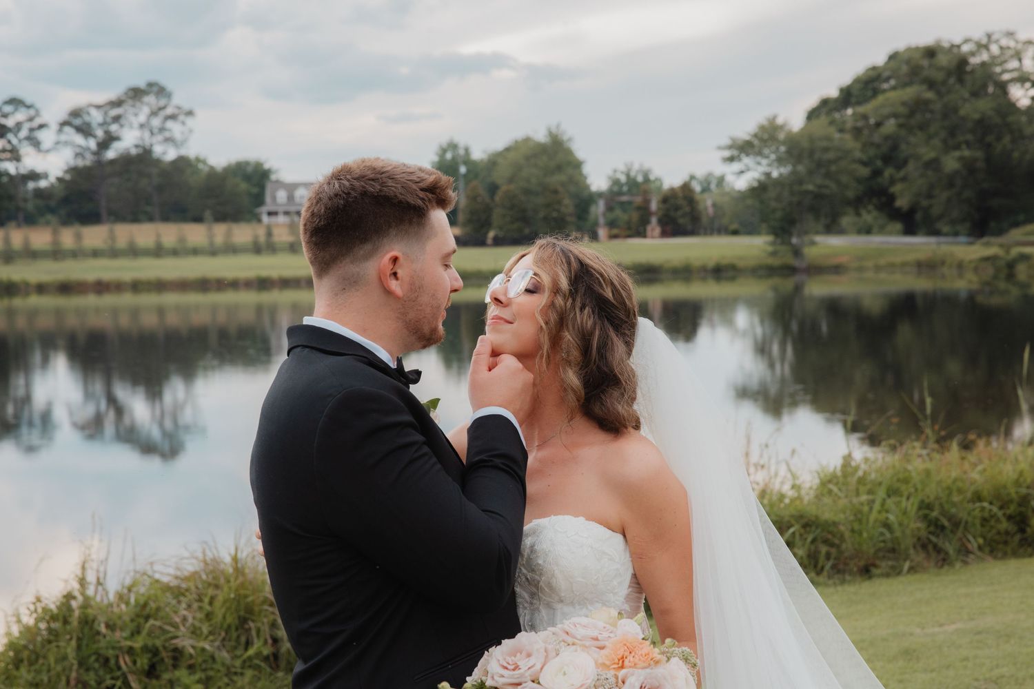 Romantic couple sharing a tender moment by a serene lake at their outdoor wedding venue.