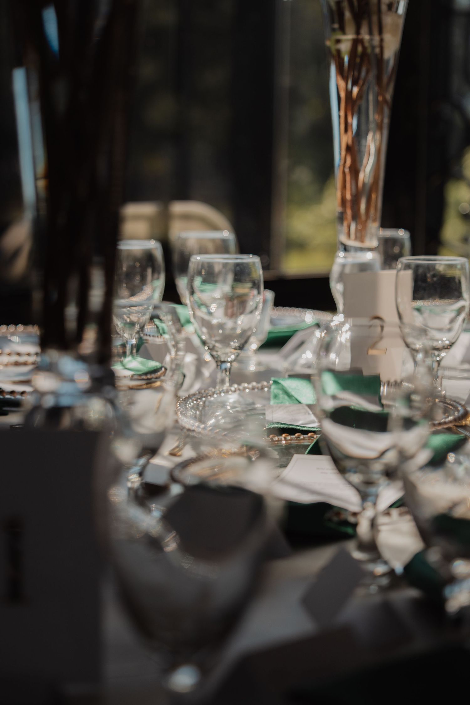 Elegant wedding reception table setting with crystal glassware and green napkins in sunlight.