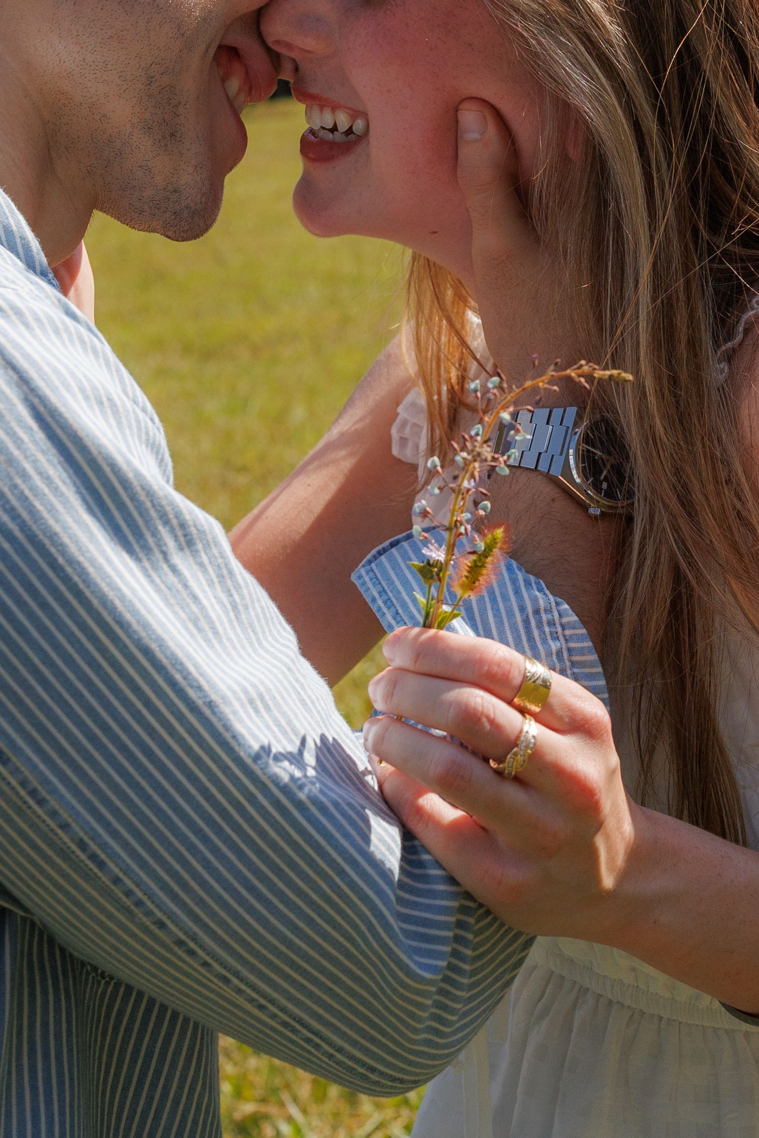 Romantic couple almost kissing outdoors in sunlight, woman holding delicate wildflowers with gold rings.