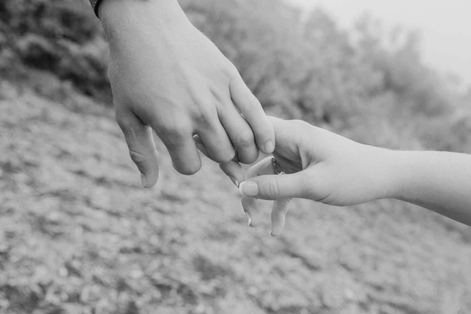Black and white close-up of two people exchanging a ring outdoors on rocky ground.