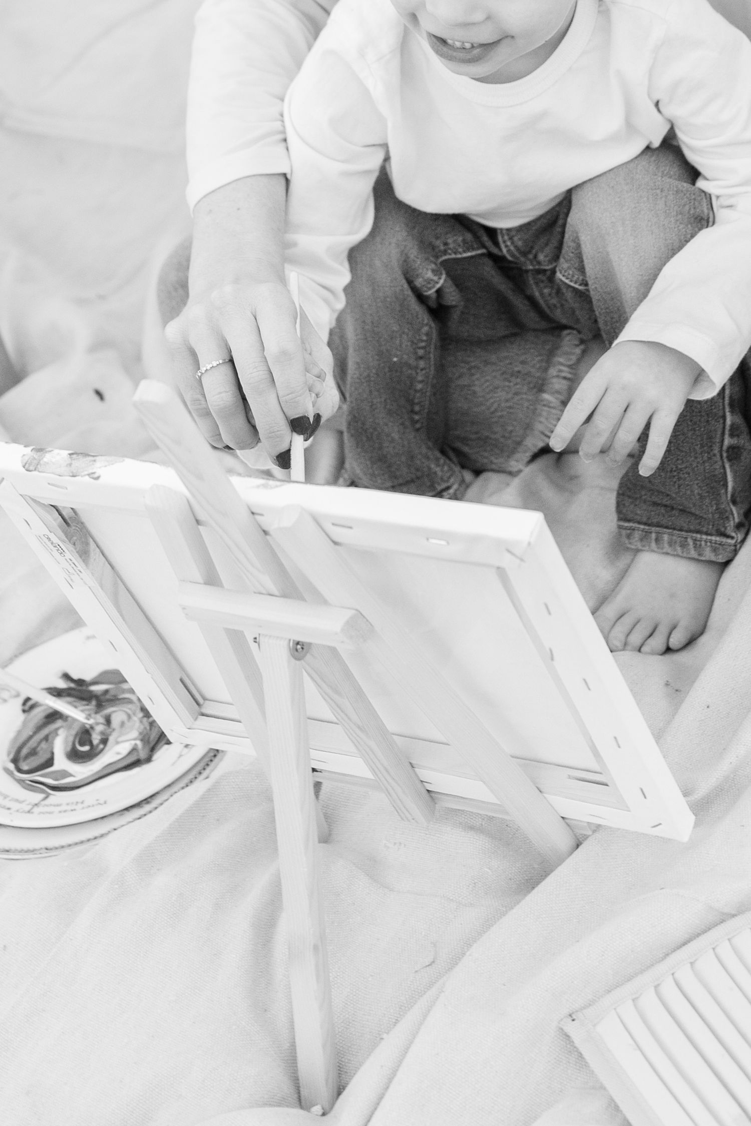 Black and white photo of a child and adult assembling a white wooden picture frame together.