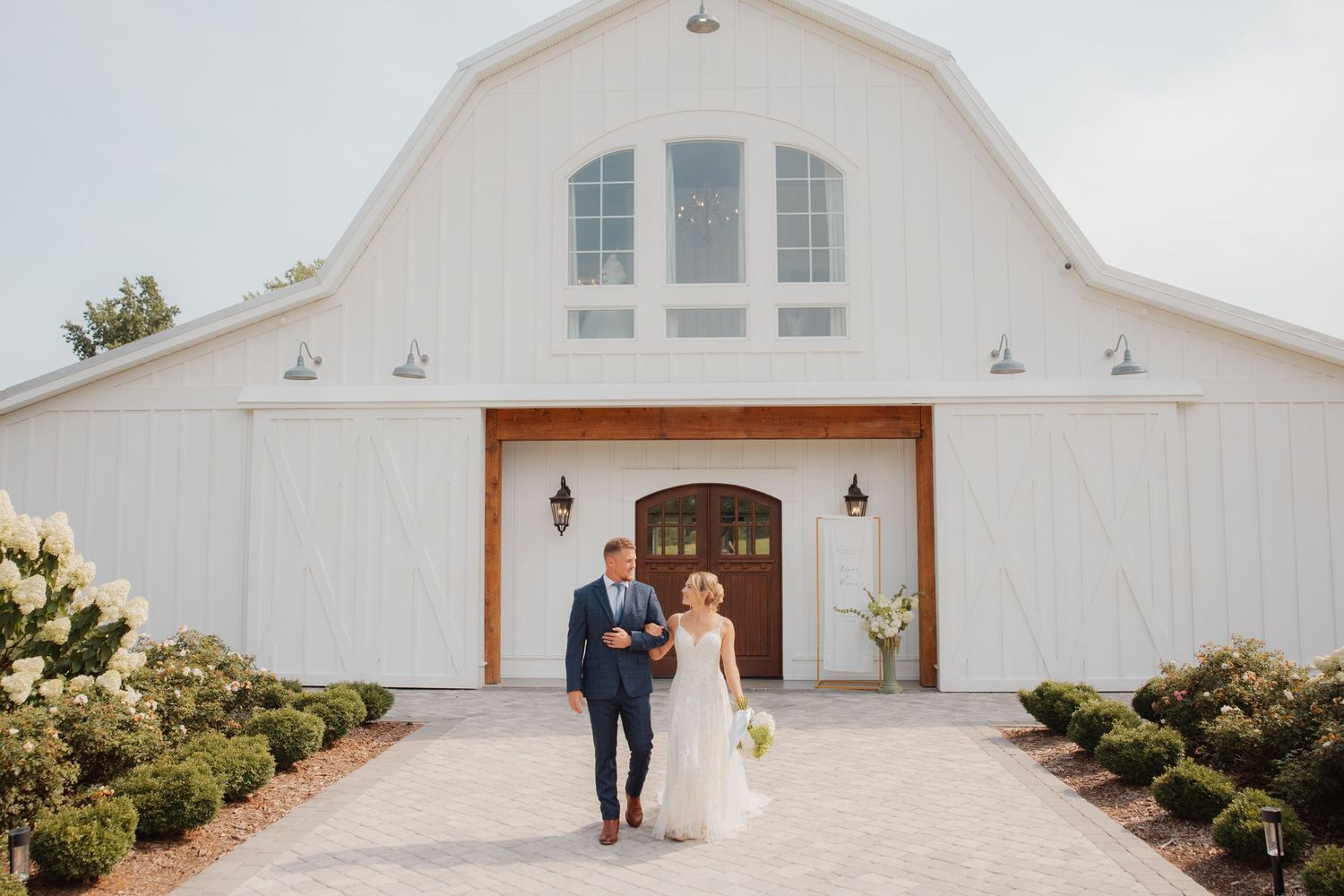 Bride and groom walking hand in hand in front of a white barn wedding venue.
