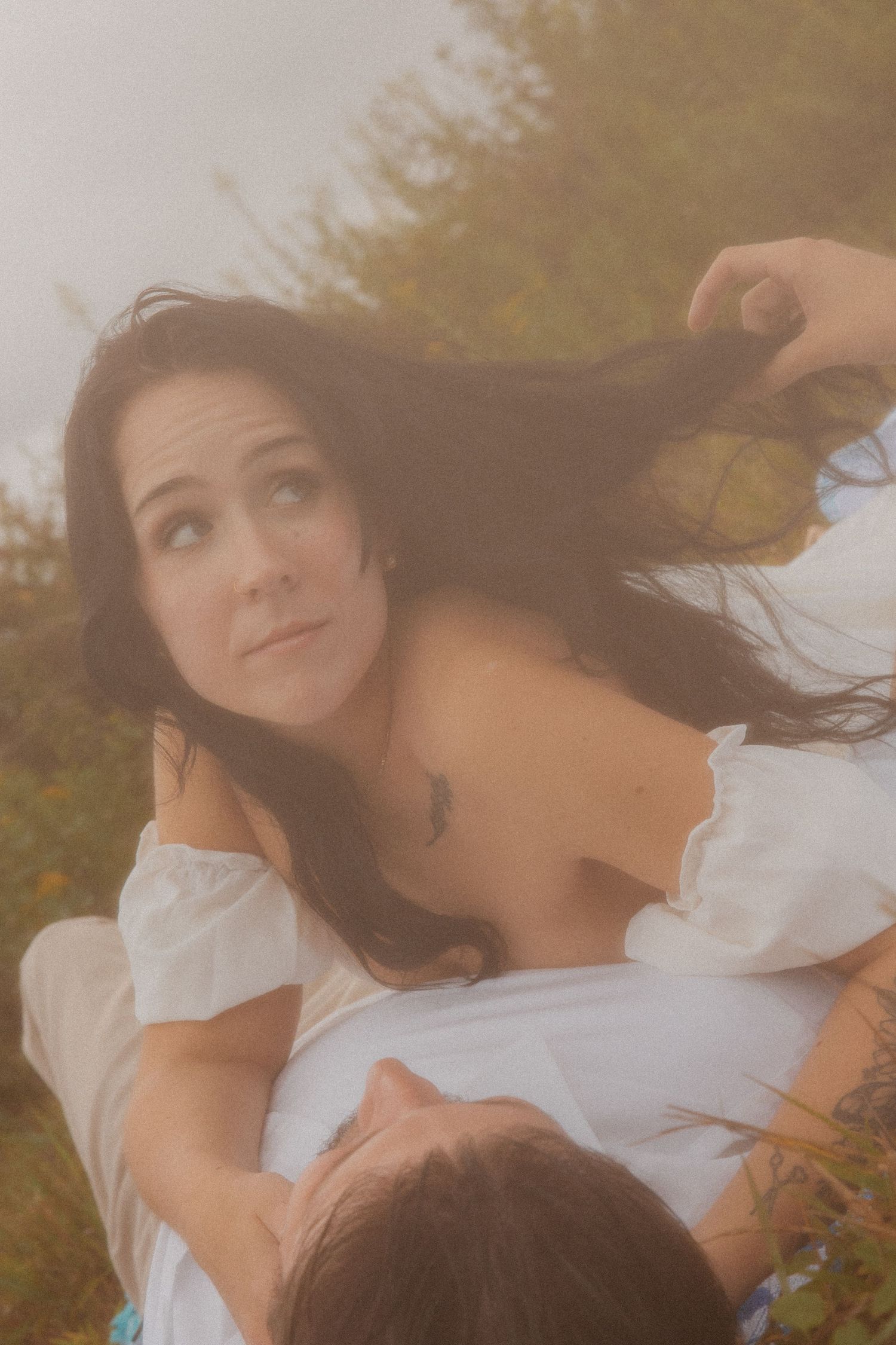 Woman in white off-shoulder dress being dipped outdoors in soft misty light.