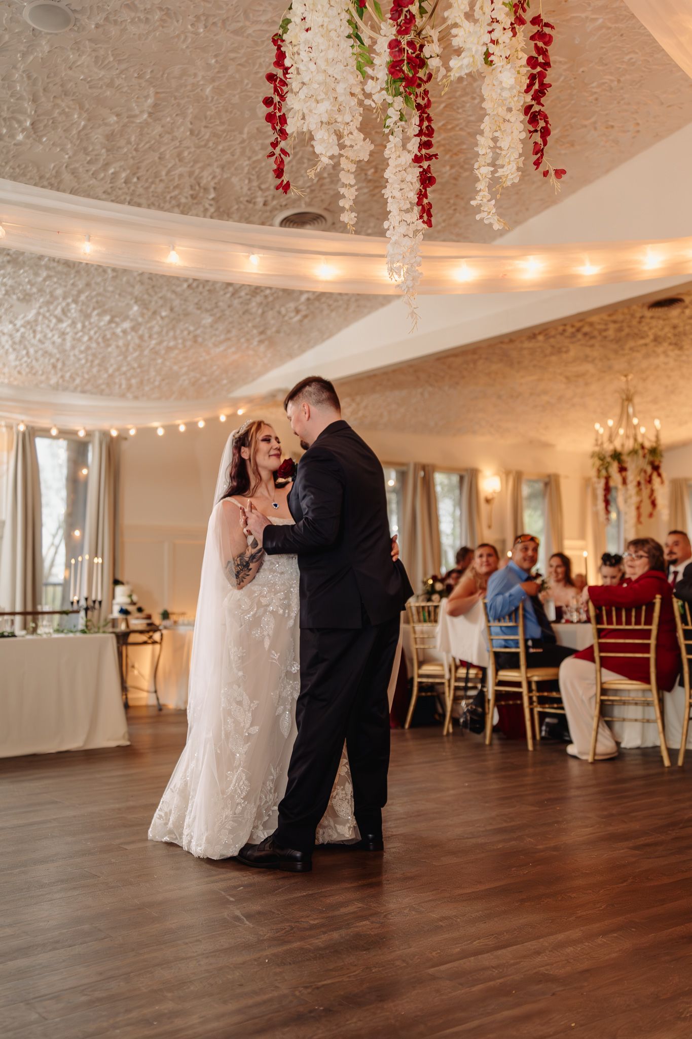 Bride and groom share their first dance under floral chandeliers in an elegant wedding reception venue.