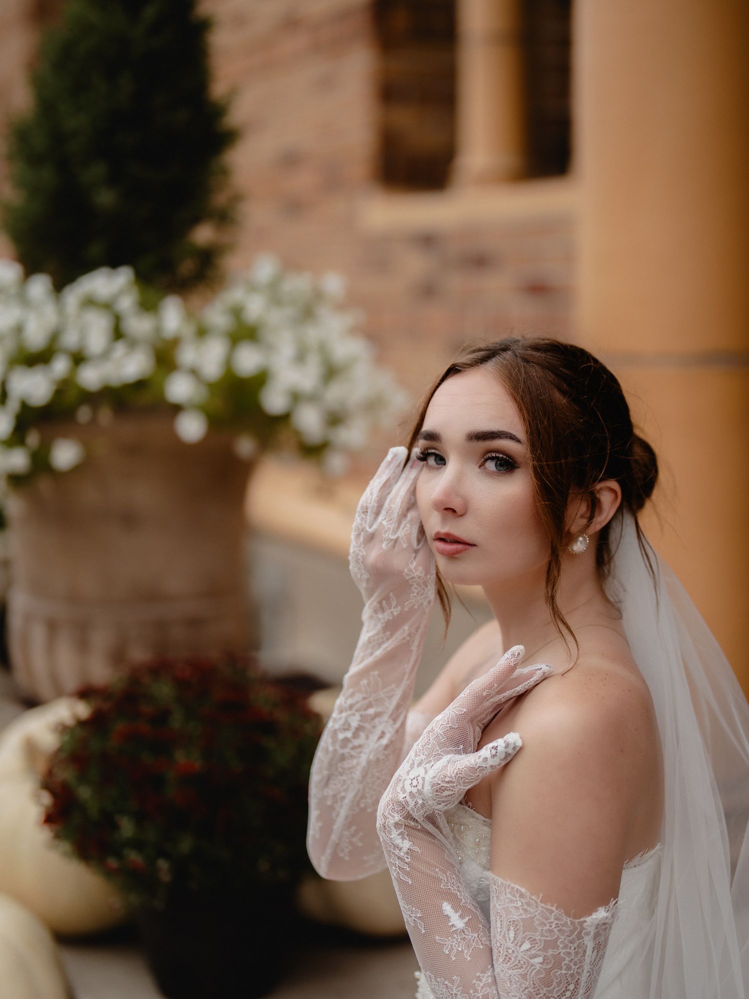 Bride in lace long sleeve wedding dress poses elegantly against stone column backdrop. Nazareth hall, grand rapids, OHIO