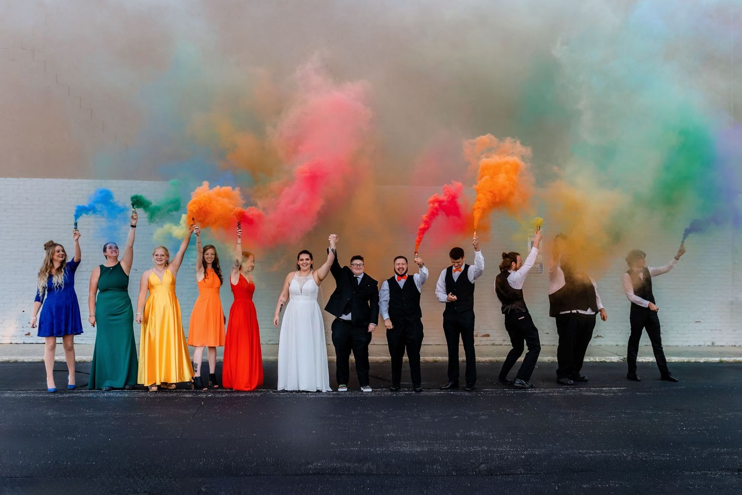 Wedding party lineup creates colorful smoke bomb photo effect against neutral background. Toledo Ohio