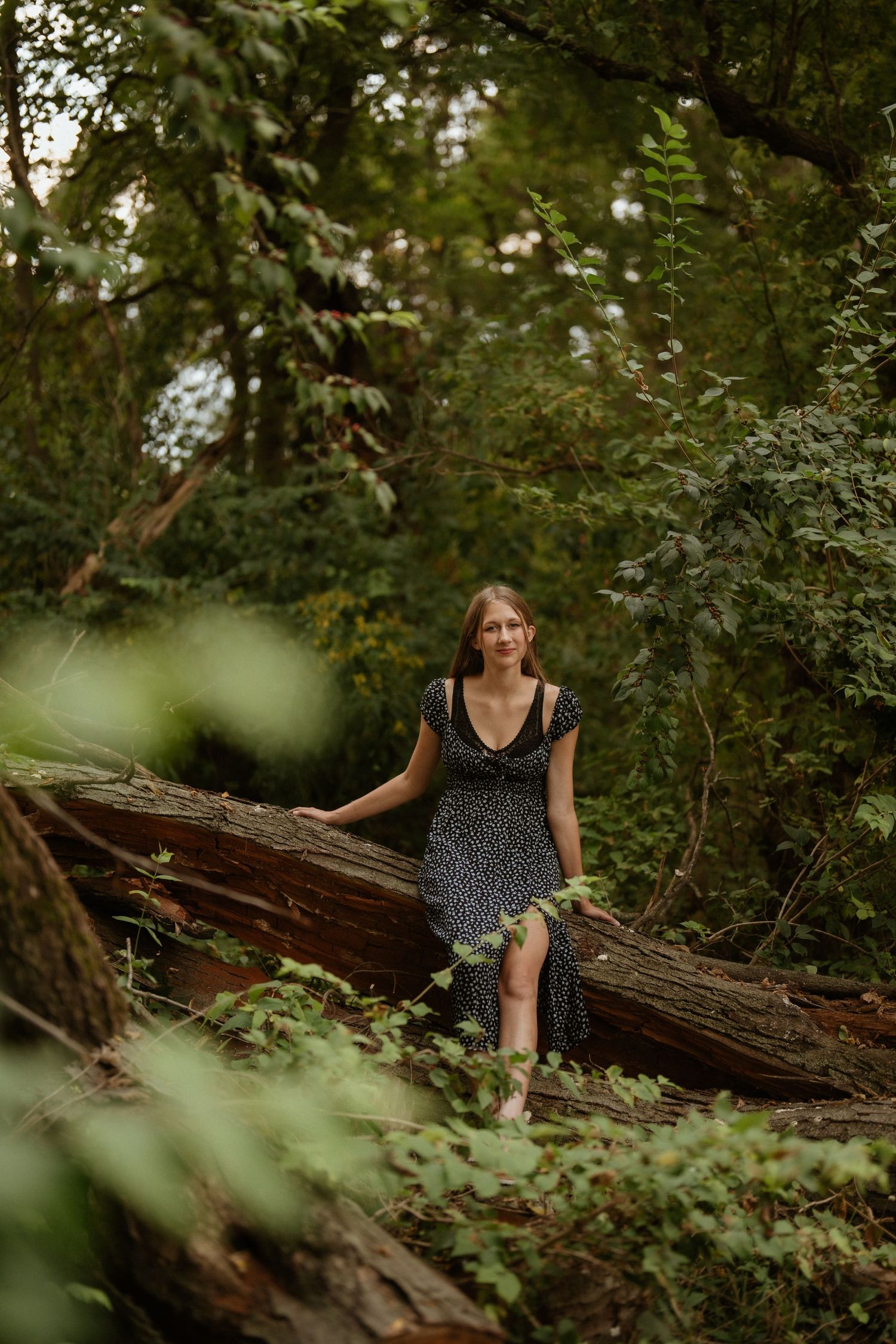 A person in a polka dot dress sits on a fallen log surrounded by lush green forest vegetation. Steyer Nature Preserve Tiffin, Oh