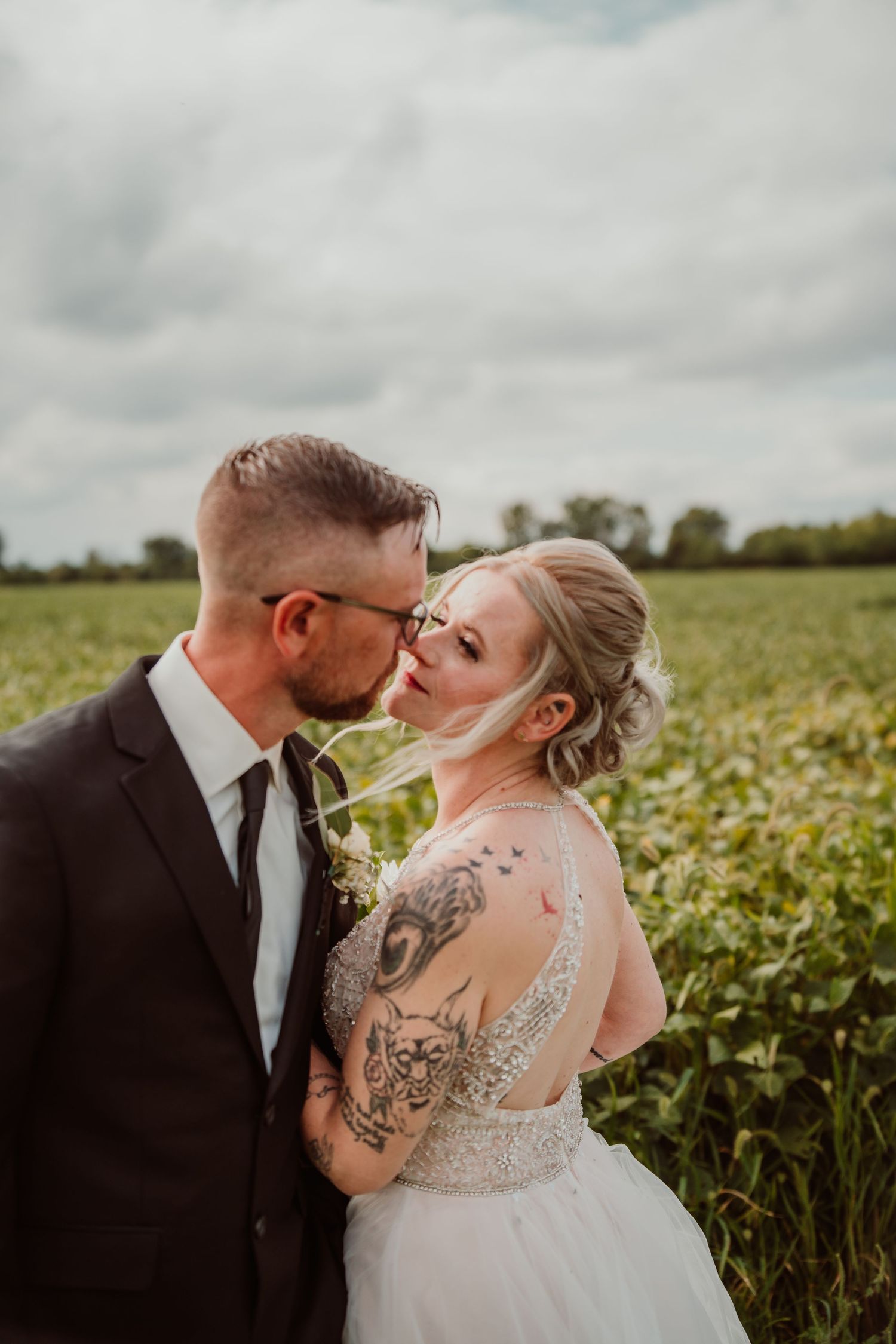 Romantic wedding portraits in a field under cloudy skies showing intimate moments. Tiffin, Ohio Wedding Venue