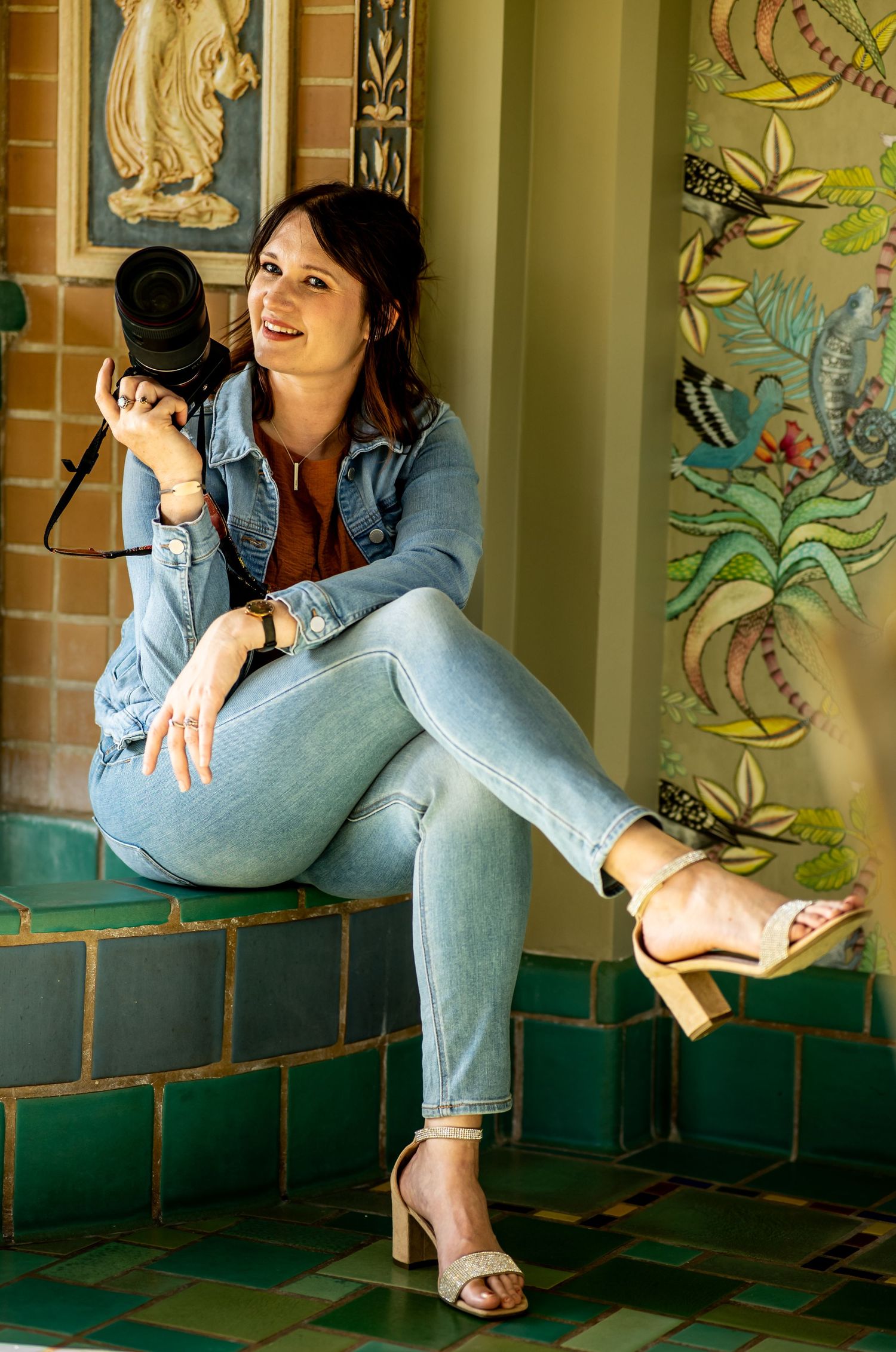 Professional photographer in casual denim outfit poses with camera against decorative tiled wall. The christy house, fremont, ohio