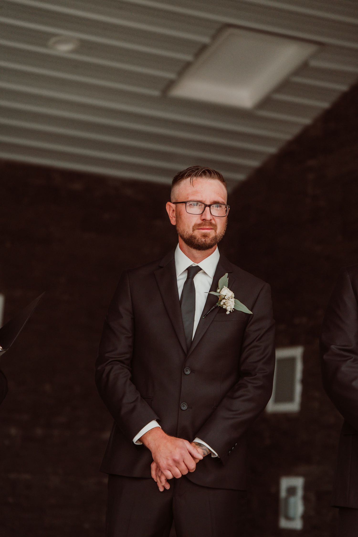 Formal portraits of a groom in a black suit and glasses against a dark background. Tiffin, Ohio Wedding Venue