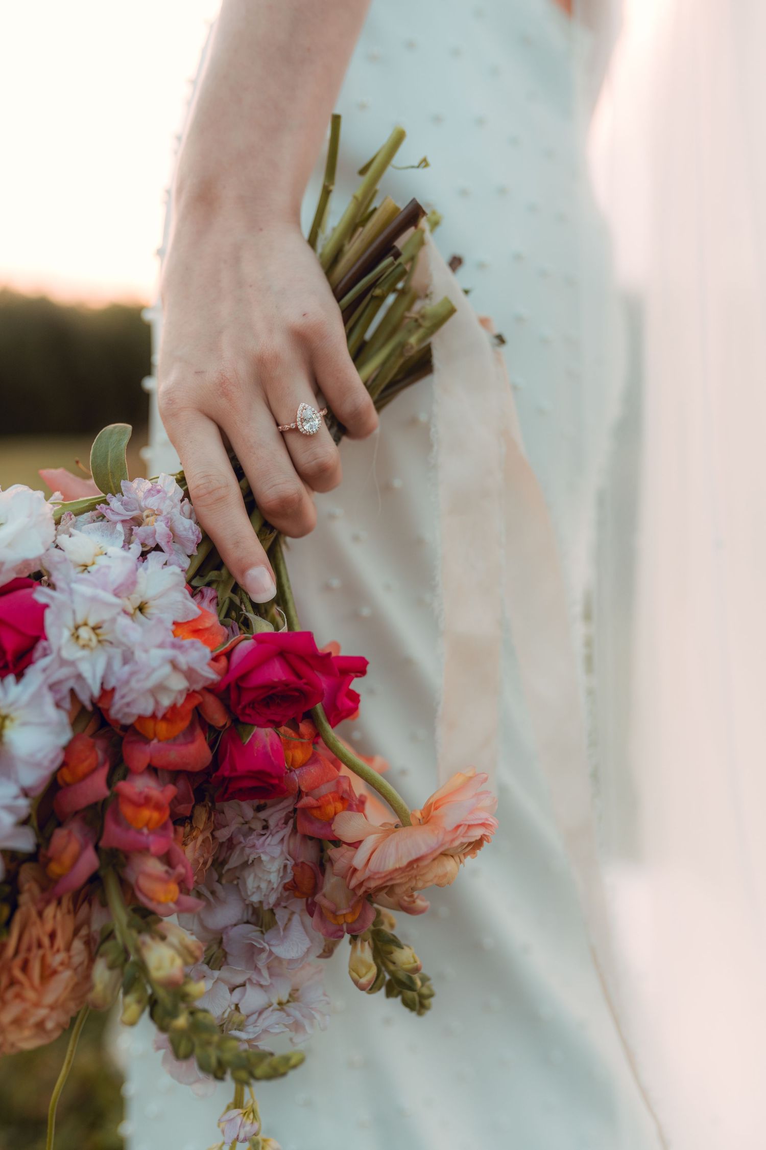 A vibrant wedding bouquet with pink and coral flowers held against a white dress. Wooster Ohio The Wellspring Wedding Venue