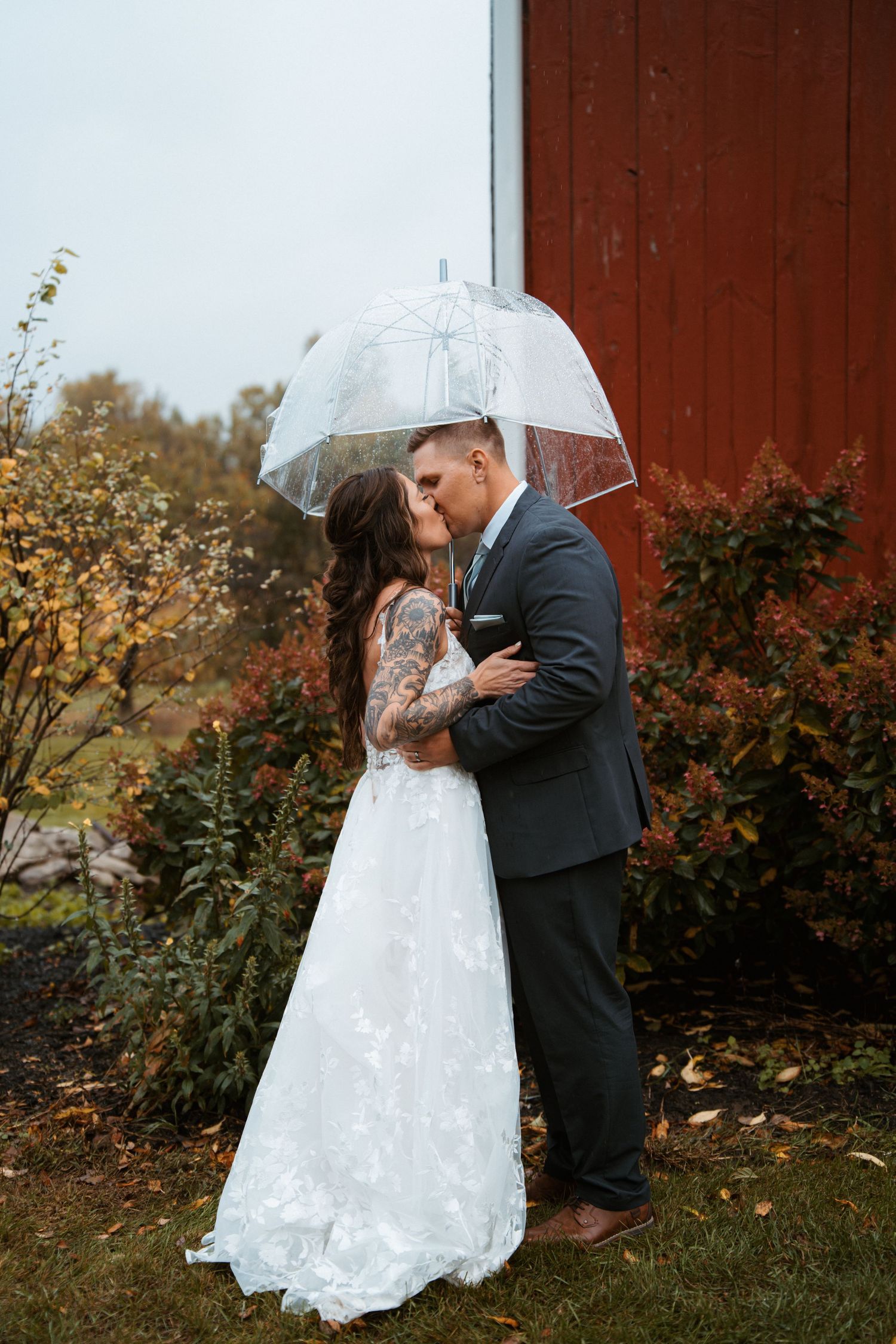 Romantic wedding couple sharing intimate moments under a clear umbrella near a red barn. Delta, Ohio wedding venue
