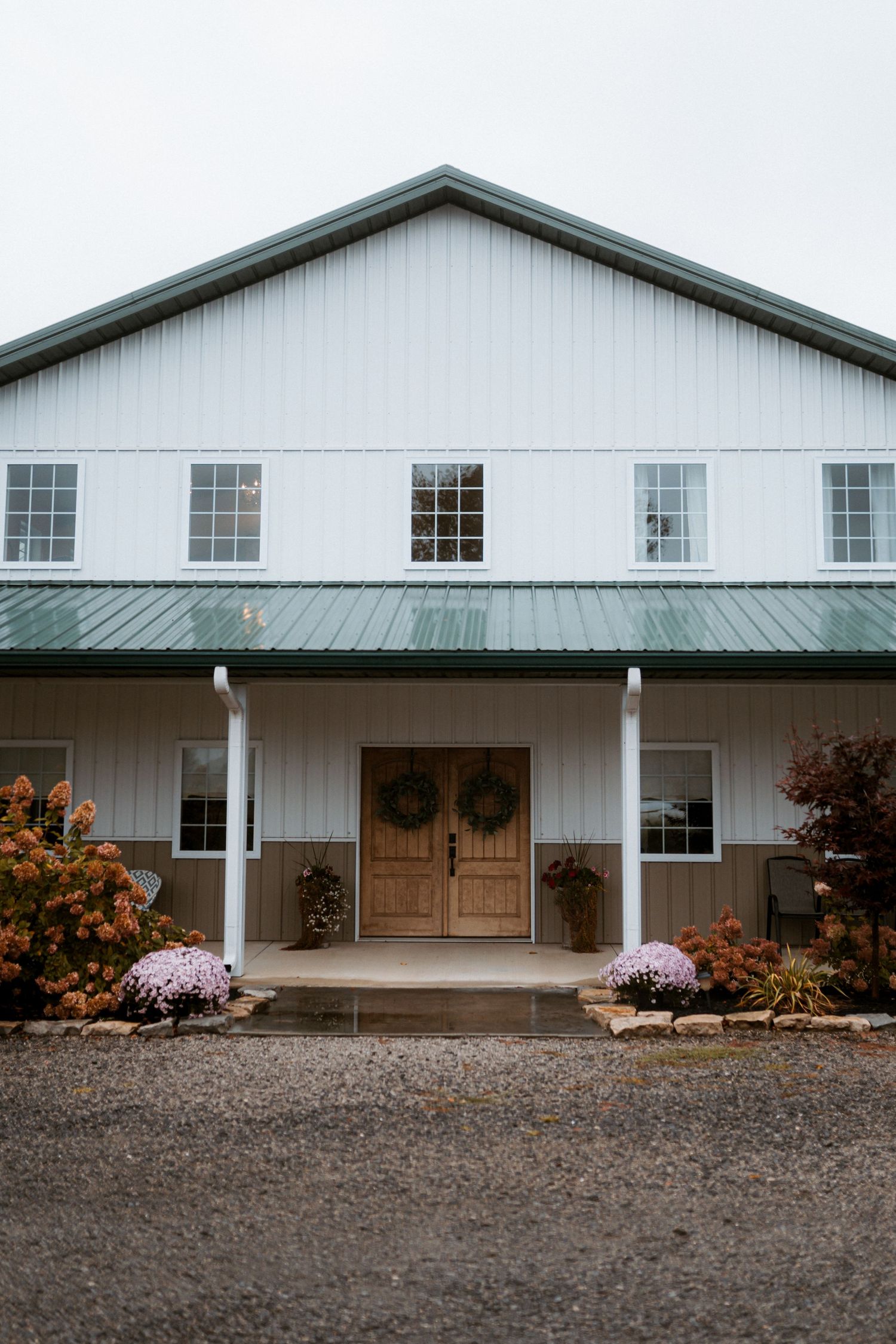 Modern white barn venue with metal roof and wooden doors decorated with floral wreaths. Delta, Ohio wedding venue