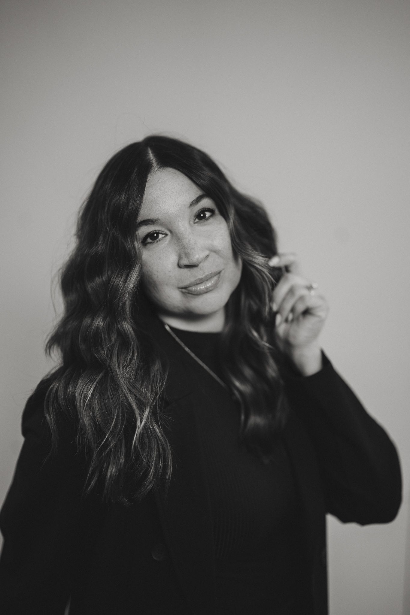 Black and white portrait of a young woman with long wavy hair smiling softly while touching her hair.