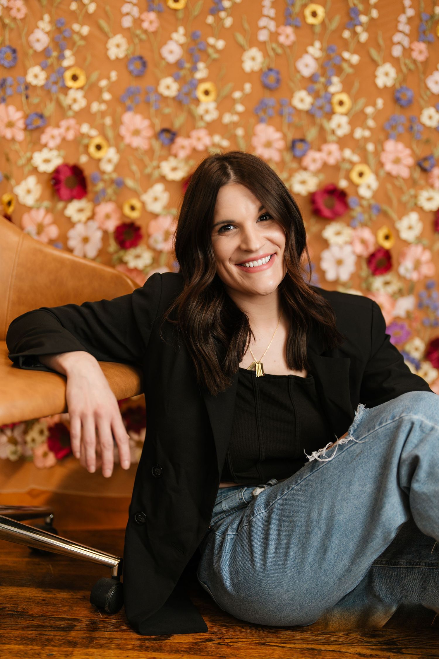 Lifestyle photos against a floral wallpaper backdrop wearing casual denim and black top. Fremont, Ohio Hair Salon