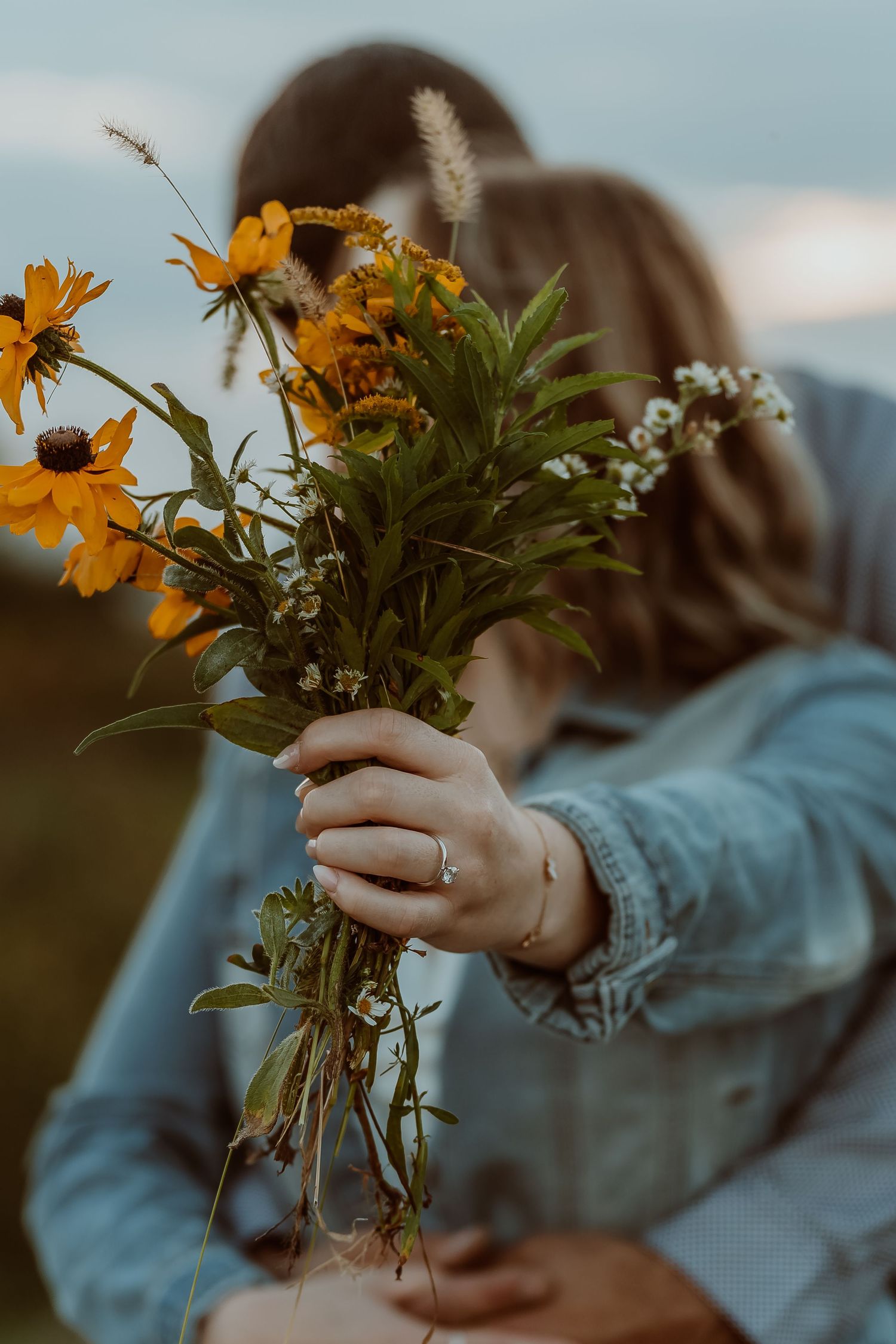A person in a denim jacket holds a bouquet of vibrant yellow wildflowers in a meadow at sunset. Lindsey ohio Wilson Nature Preserve