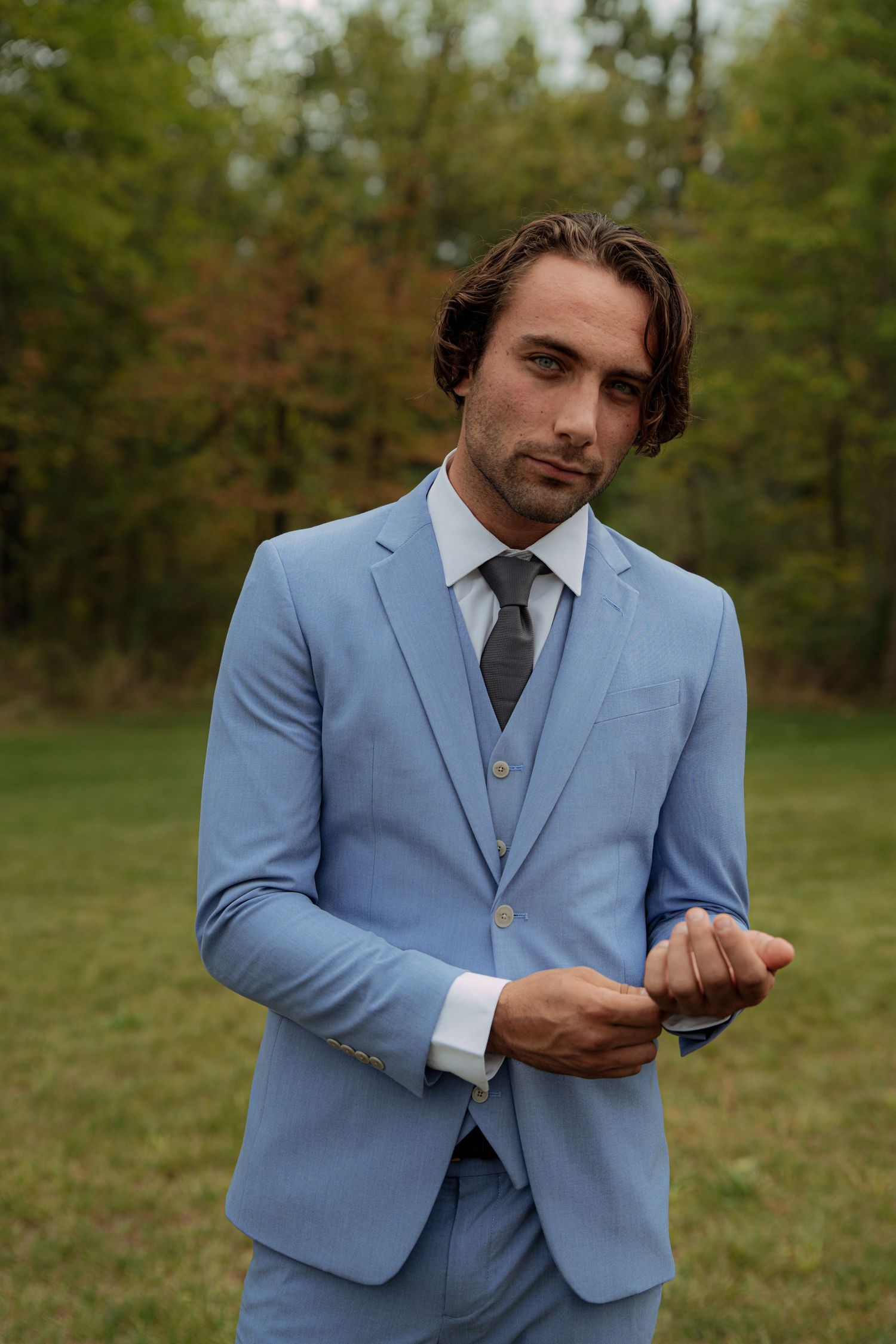 Groom in powder blue suit adjusting his tie outdoors. Wooster Ohio The Wellspring Wedding Venue