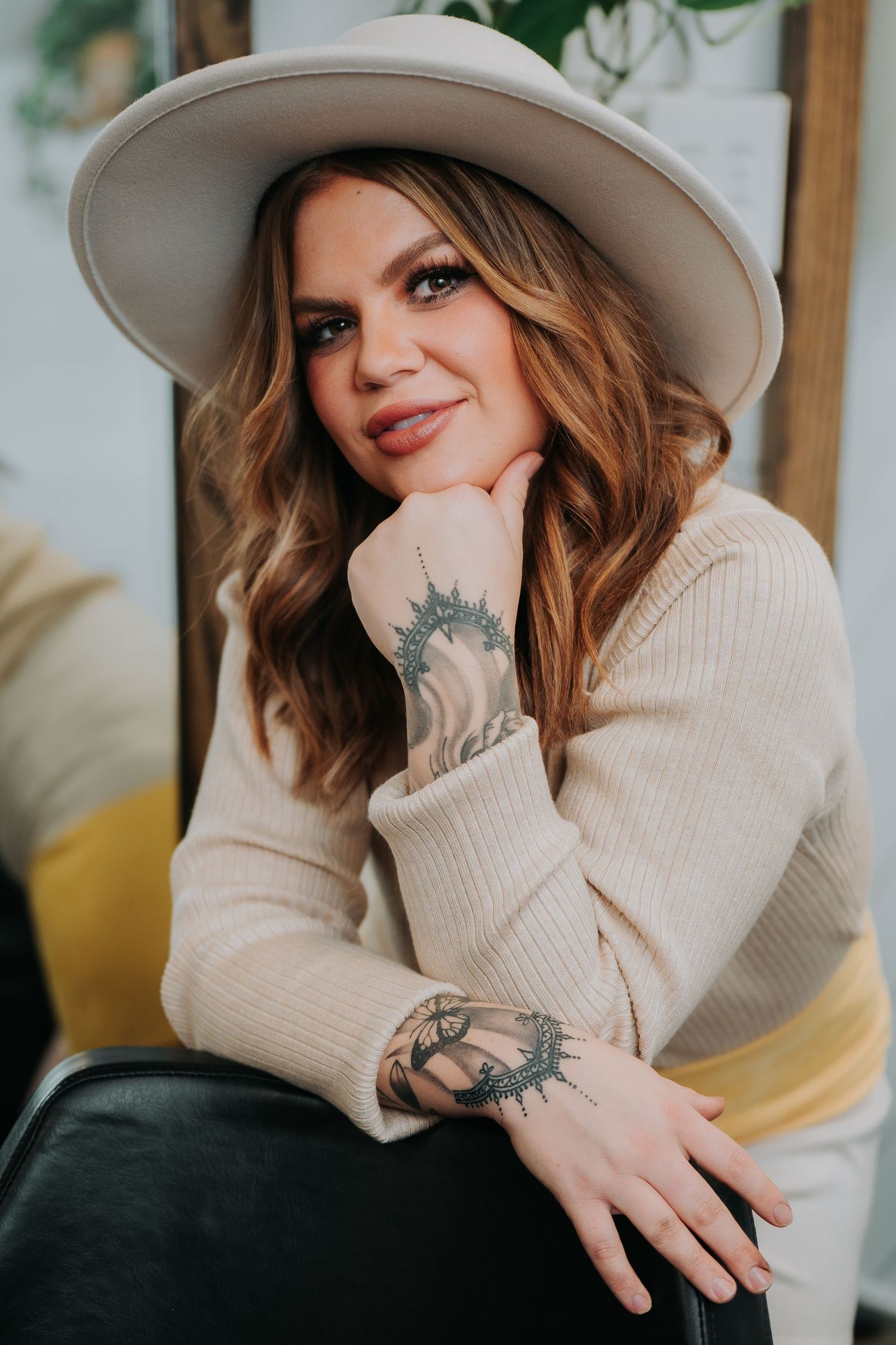 Lifestyle photos featuring a beige sweater, wide-brim hat, and visible tattoo art. Fremont, Ohio Hair Salon