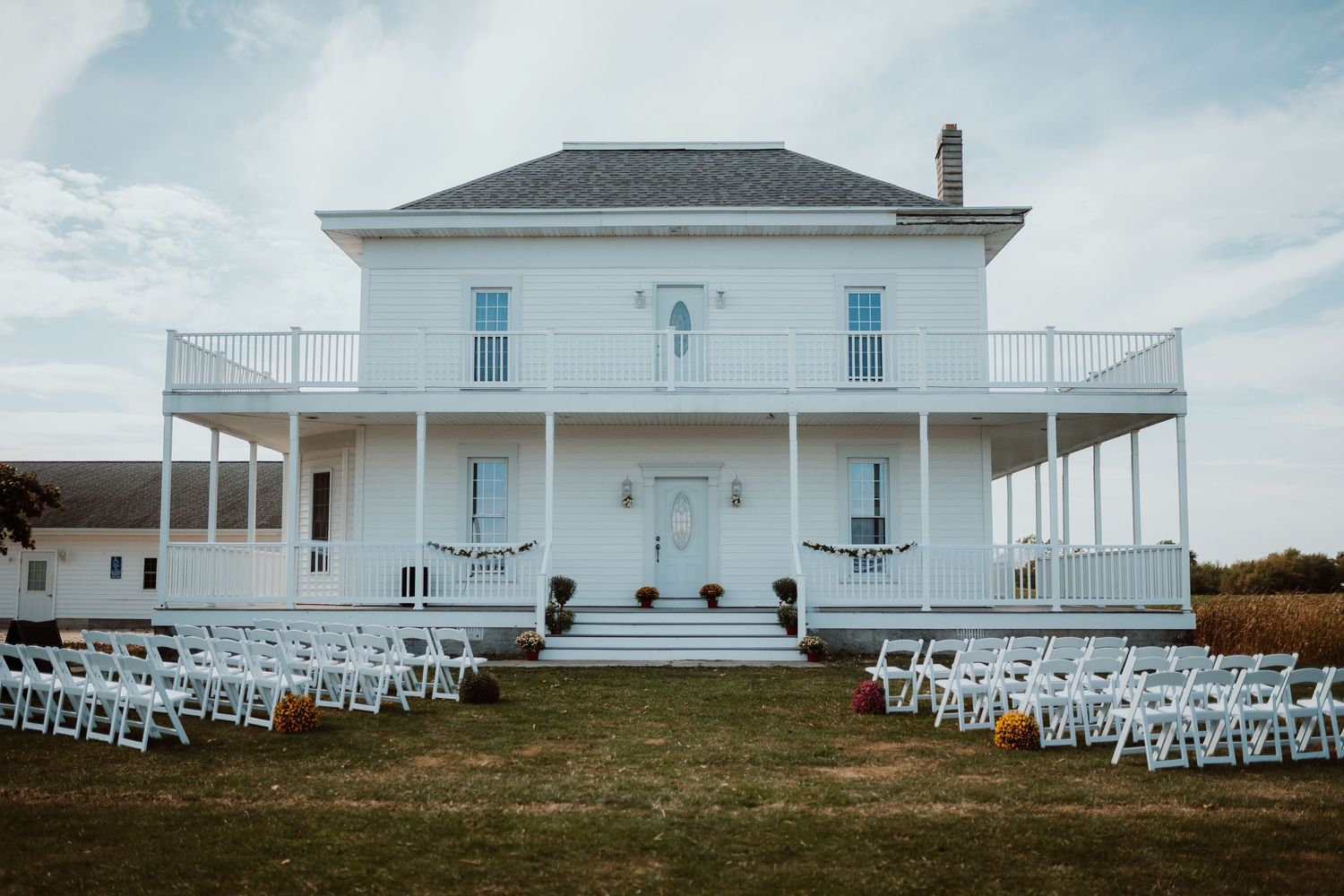 White colonial-style venue with wraparound porch and rows of chairs set up for outdoor event. Tiffin, Ohio Wedding Venue