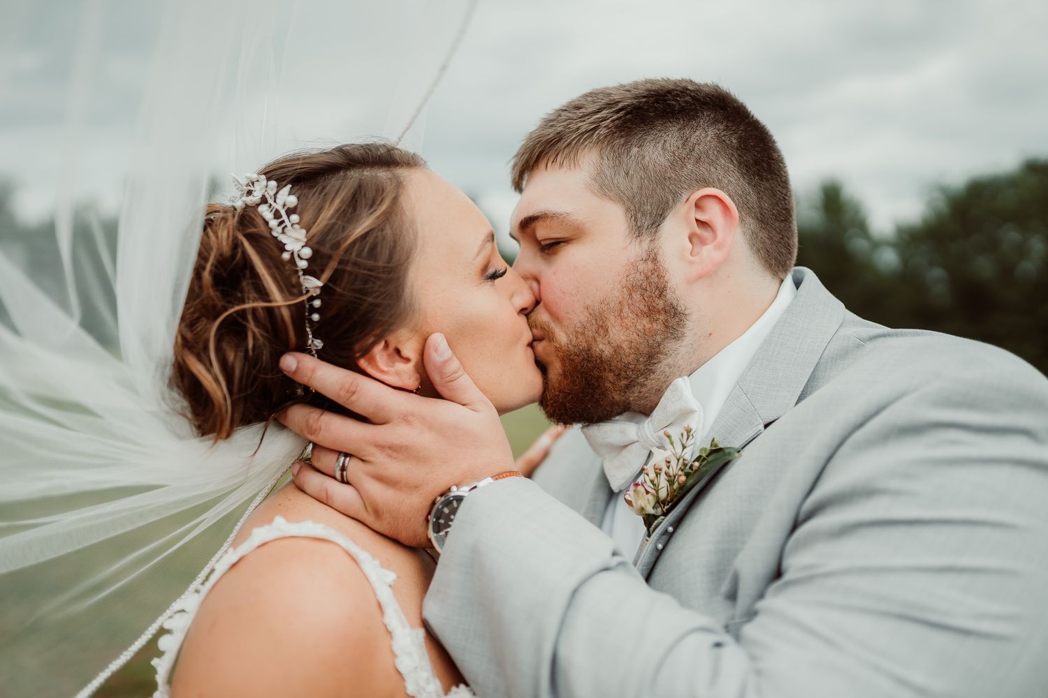 Romantic wedding kiss with flowing veil and gray suit against cloudy sky. Marina Sandusky Ohio
