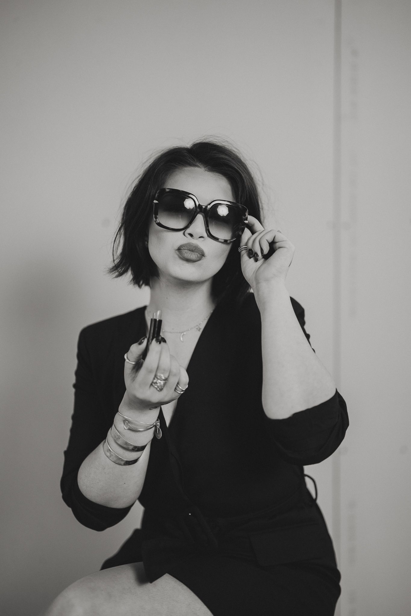 Black and white photo of a stylish woman in sunglasses and black blazer posing confidently.
