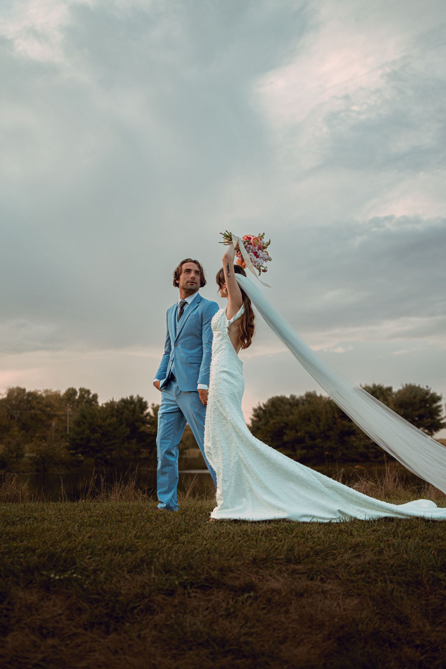A romantic wedding photo of a couple standing in a field at sunset with a flowing white dress and veil. Wooster Ohio The Wellspring Wedding