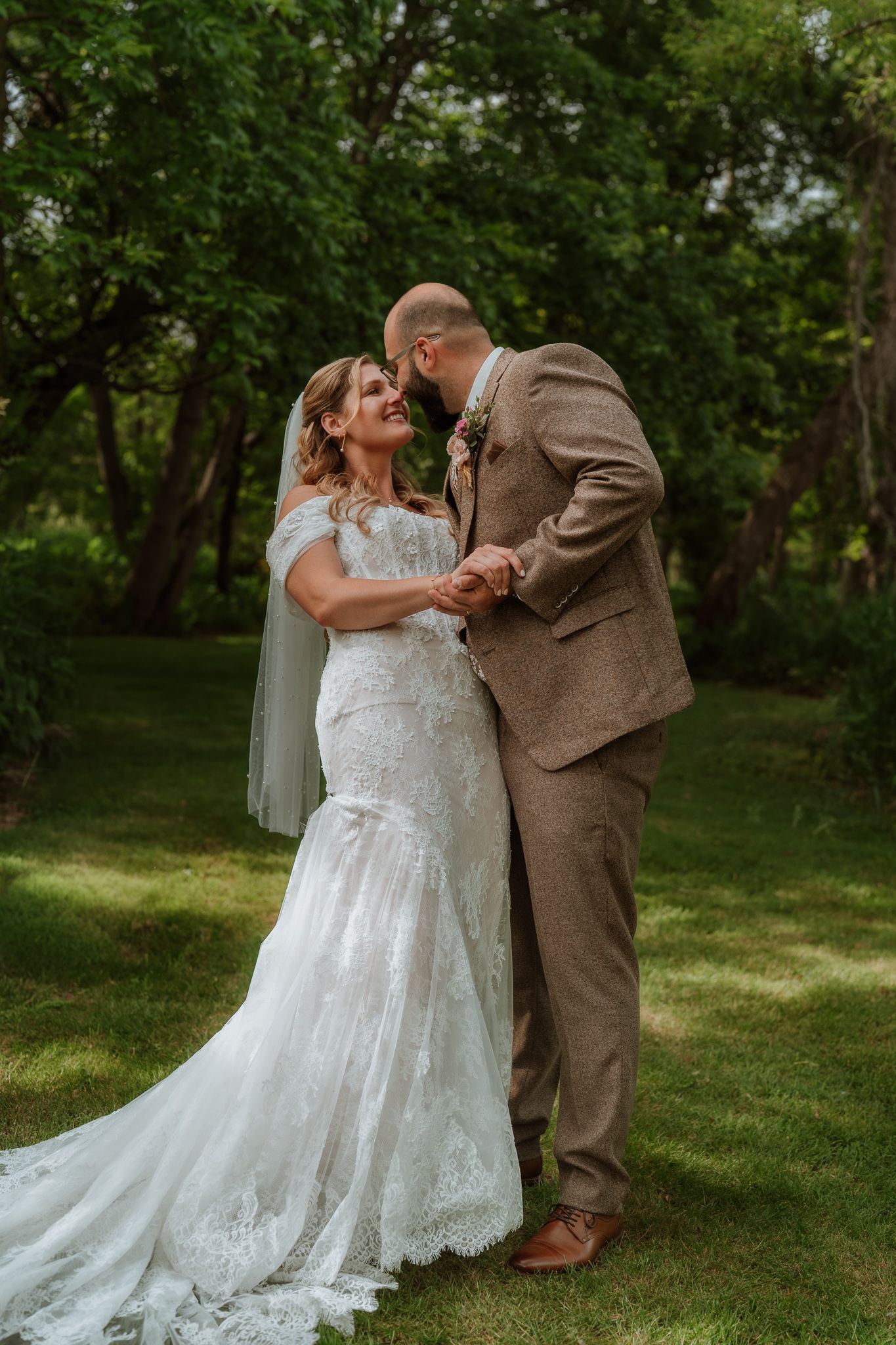 A bride and groom share a romantic moment outdoors, surrounded by lush green trees on their wedding day.