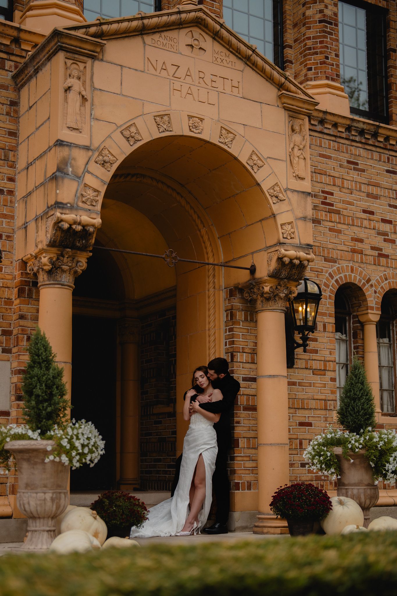 Wedding couple shares intimate moment under brick archway decorated with floral arrangements. Nazareth hall, grand rapids, OHIO